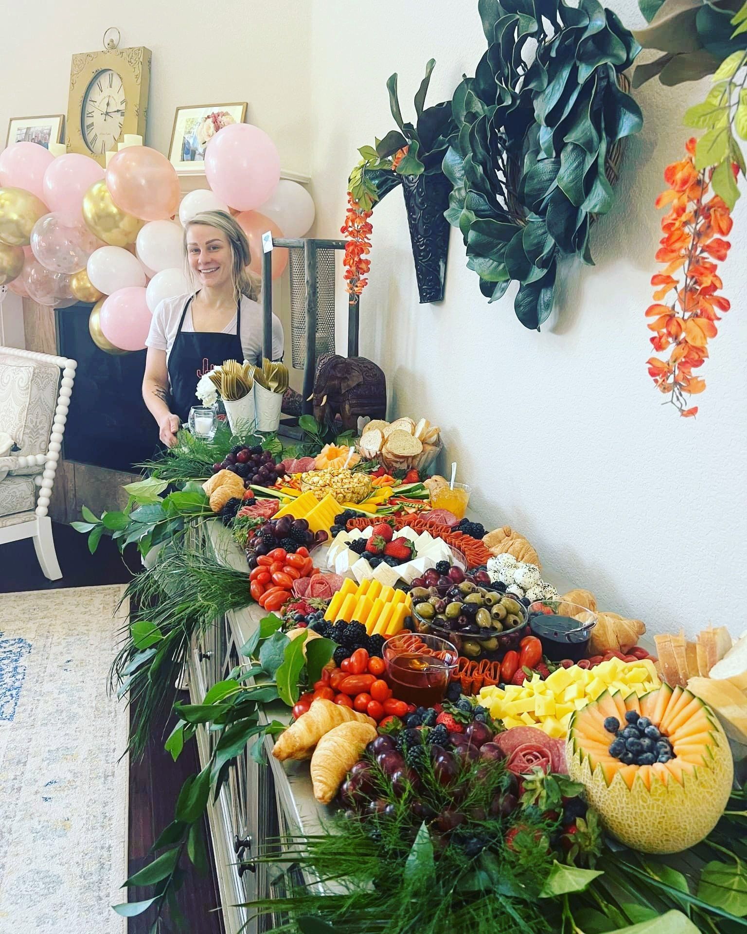 A woman is standing in front of a table filled with fruits and vegetables.
