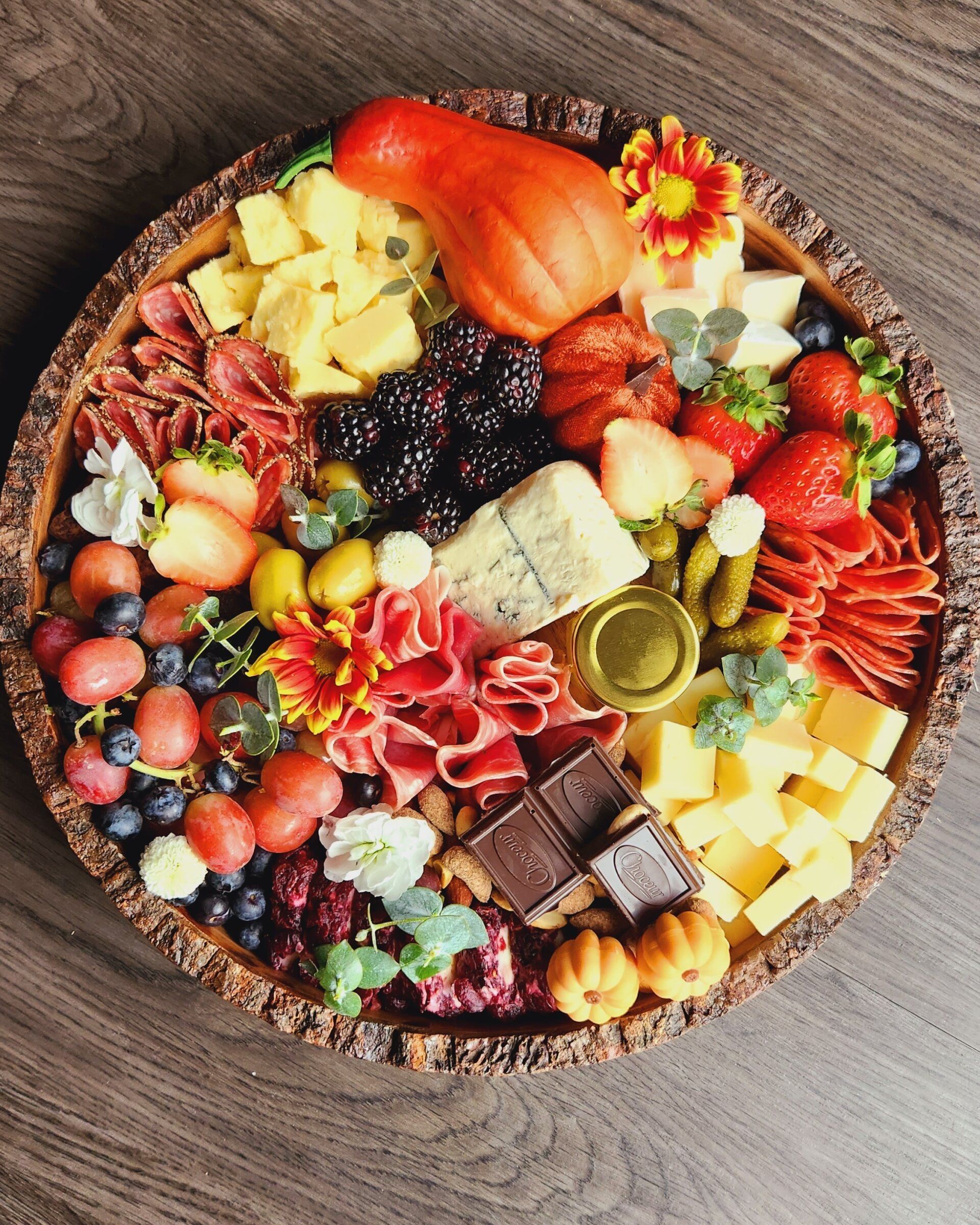 A wooden tray filled with a variety of fruits and cheeses on a wooden table.