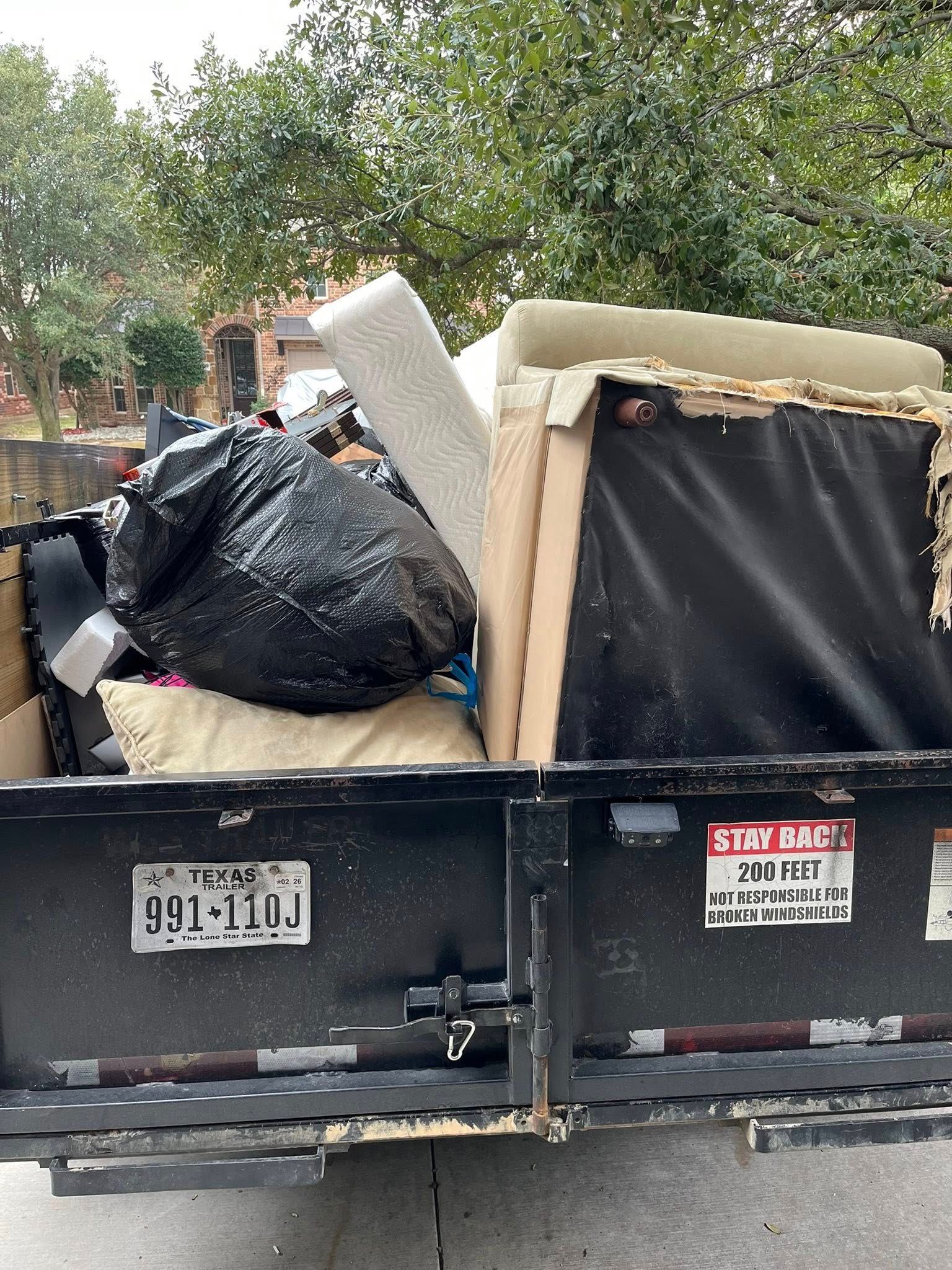 A truck bed filled with trash, including a large black bag, foam, and a chair. Texas license plate visible.