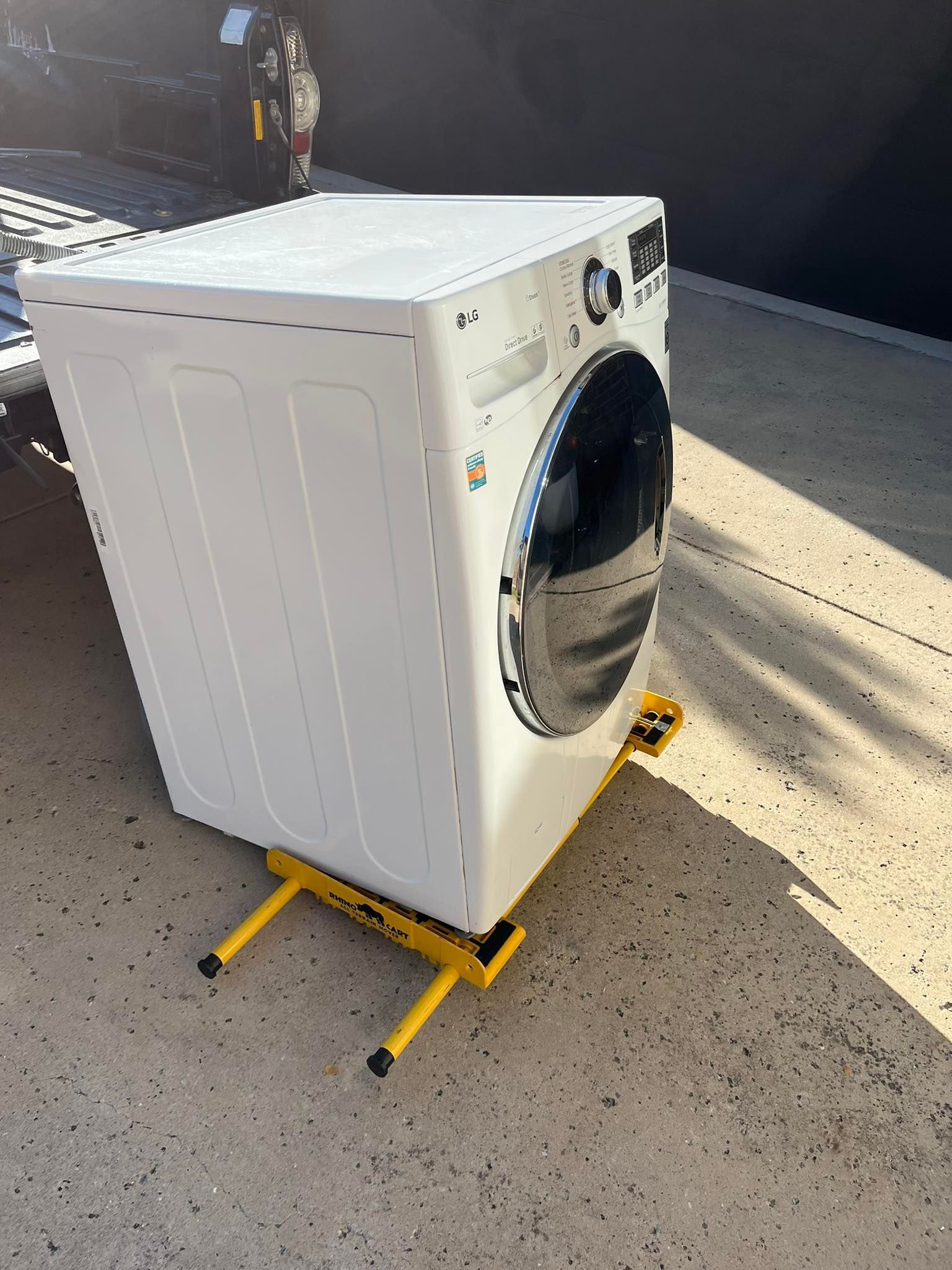 White washing machine on a yellow appliance dolly in an outdoor setting.
