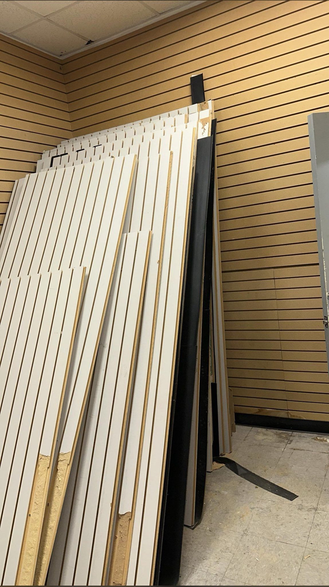 Stack of white slotted retail display panels against a wall with a pegboard design.