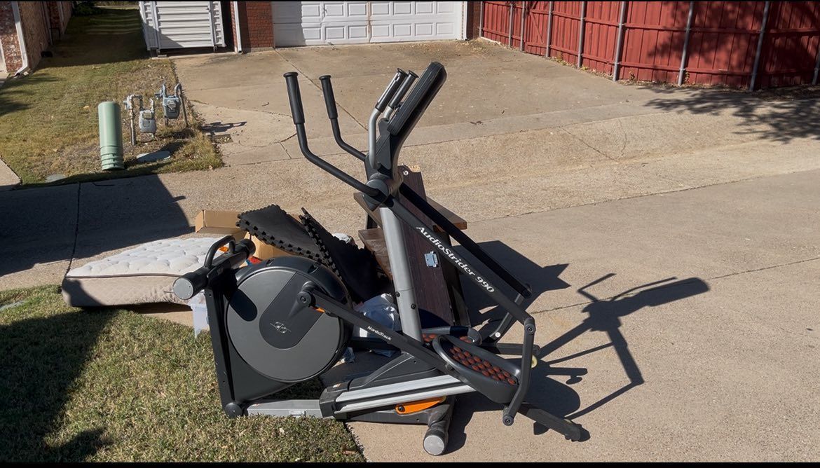 An exercise machine on the ground outdoors, next to a sidewalk and grass.