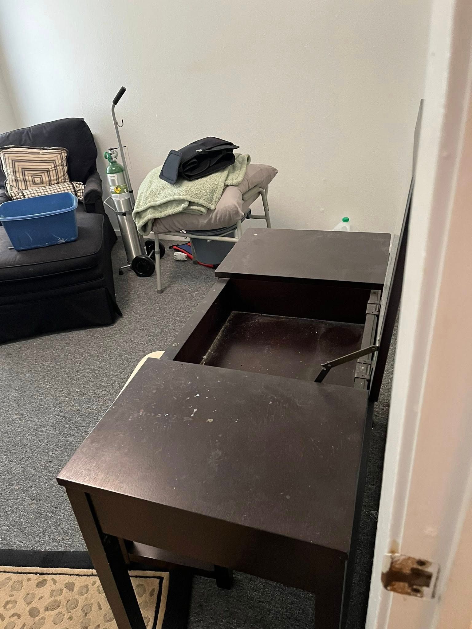 Dark wood desk with open drawers. Room with chair, vacuum, and rug.