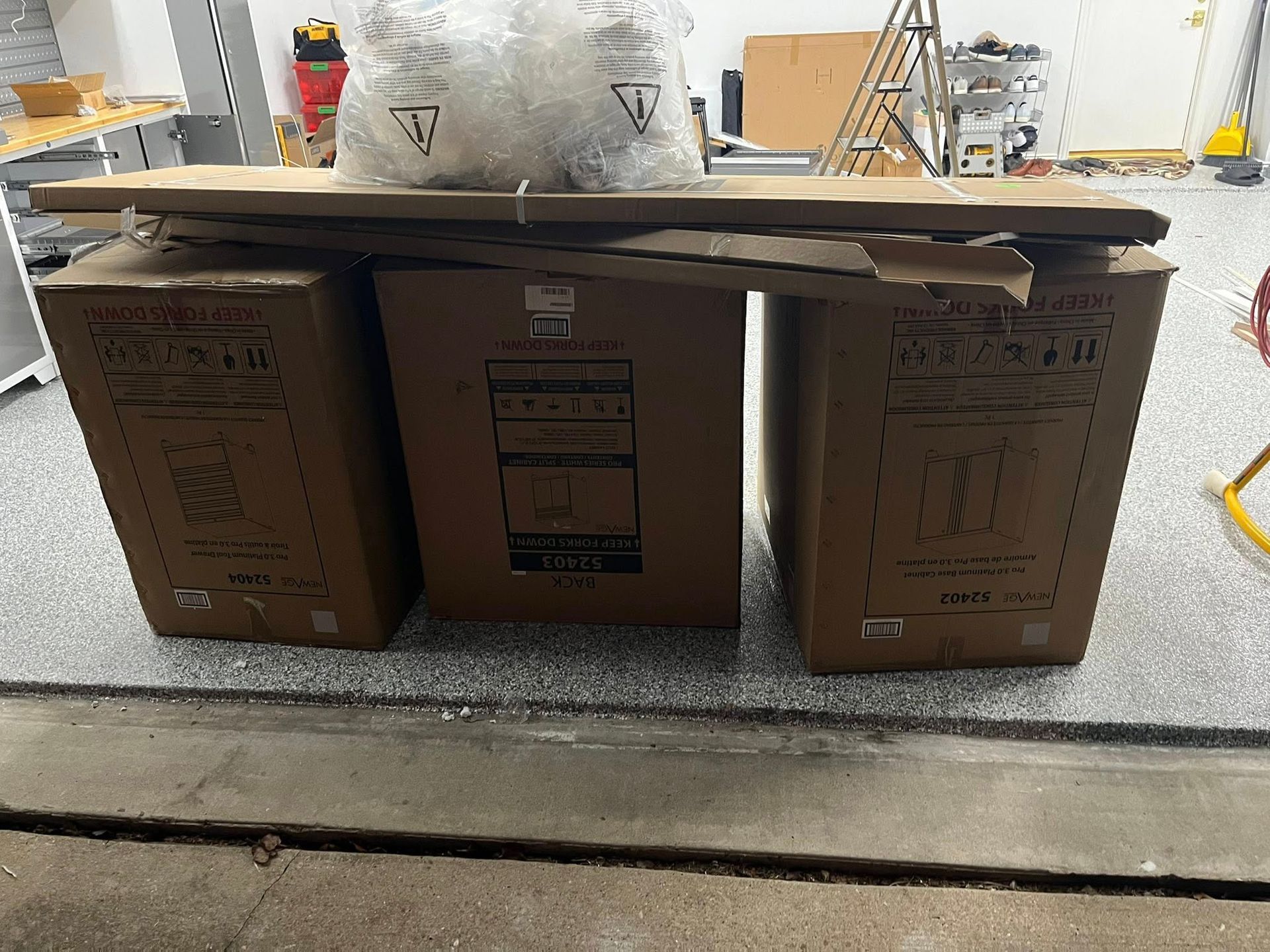 Three brown cardboard boxes stacked, with packaging materials and boards on top, in a garage.