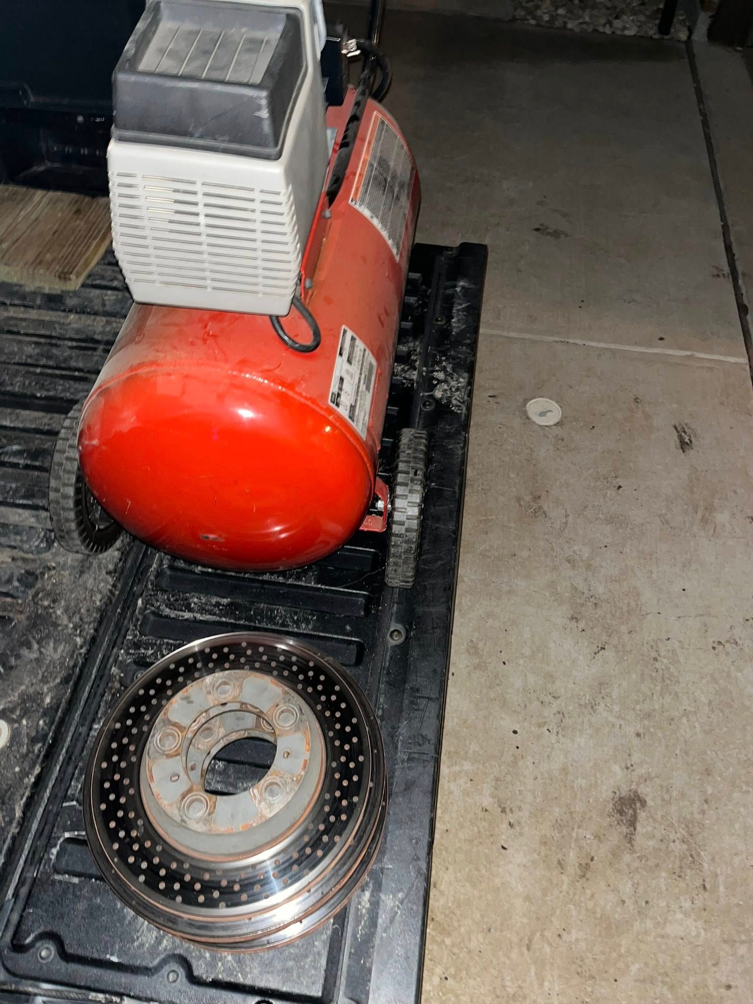 Red air compressor and brake rotor on a black utility bed.