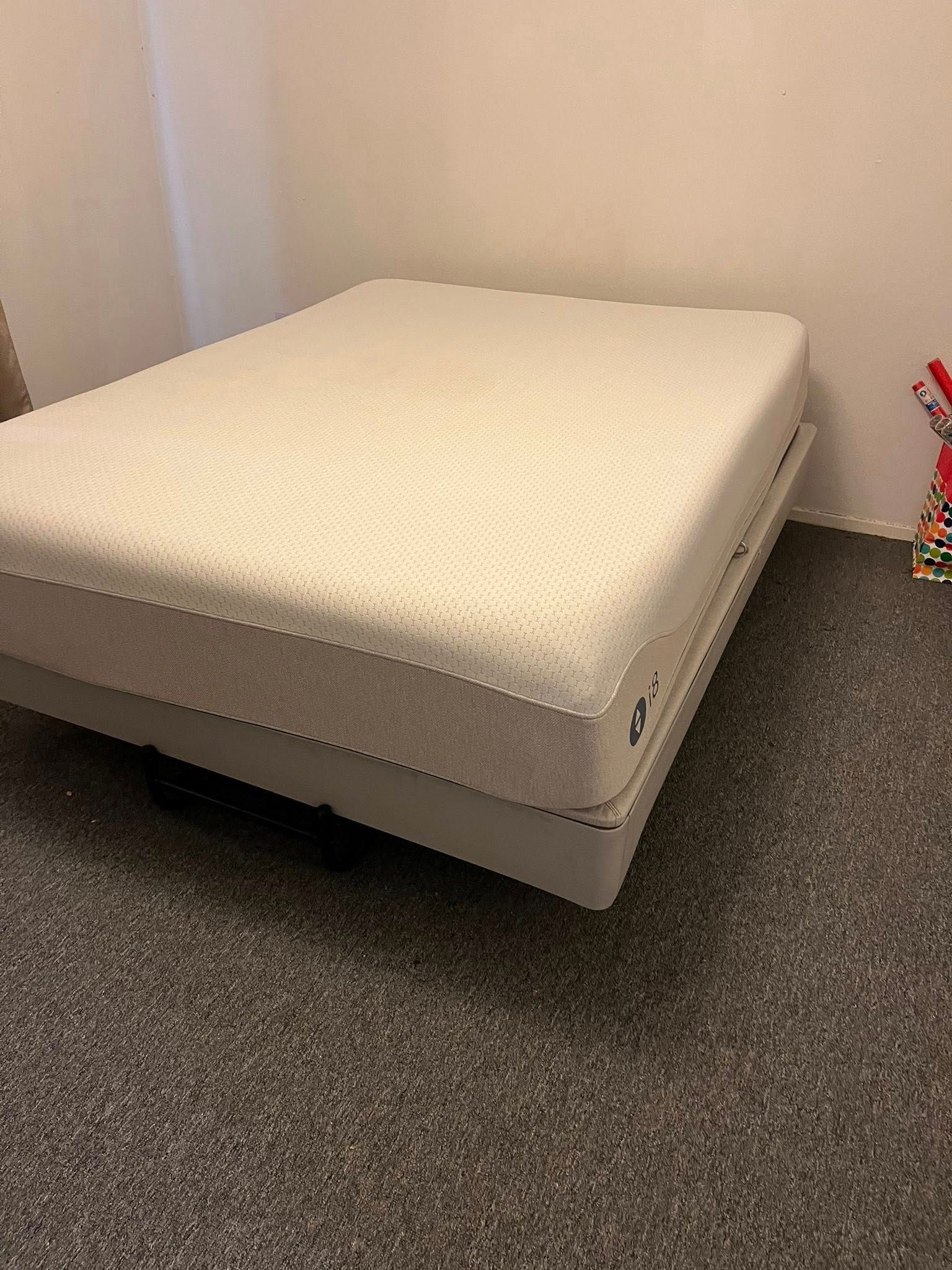 A white mattress on a gray platform bed in a room with gray carpet and white walls.