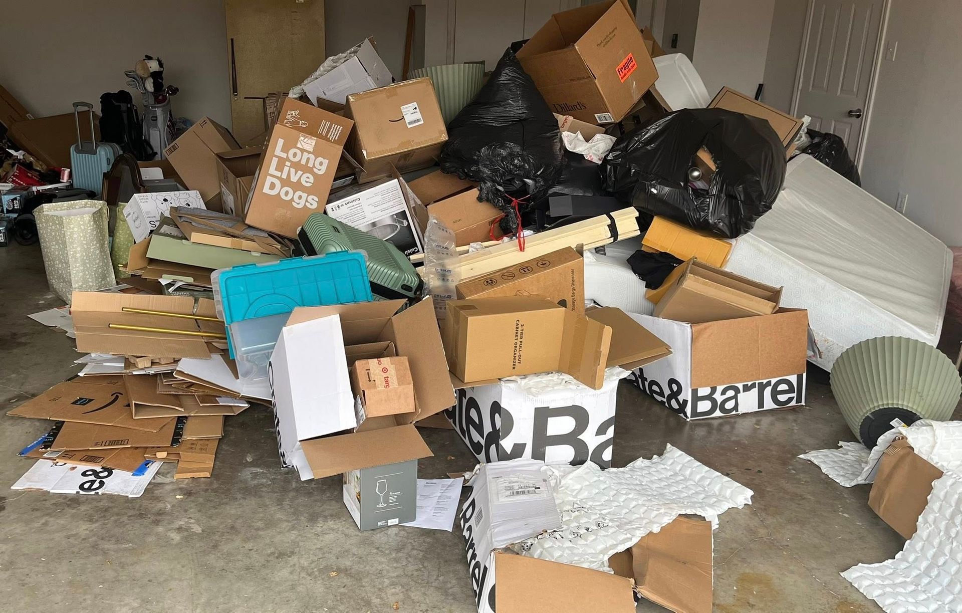 Pile of cardboard boxes, trash bags, and packing materials in a garage.