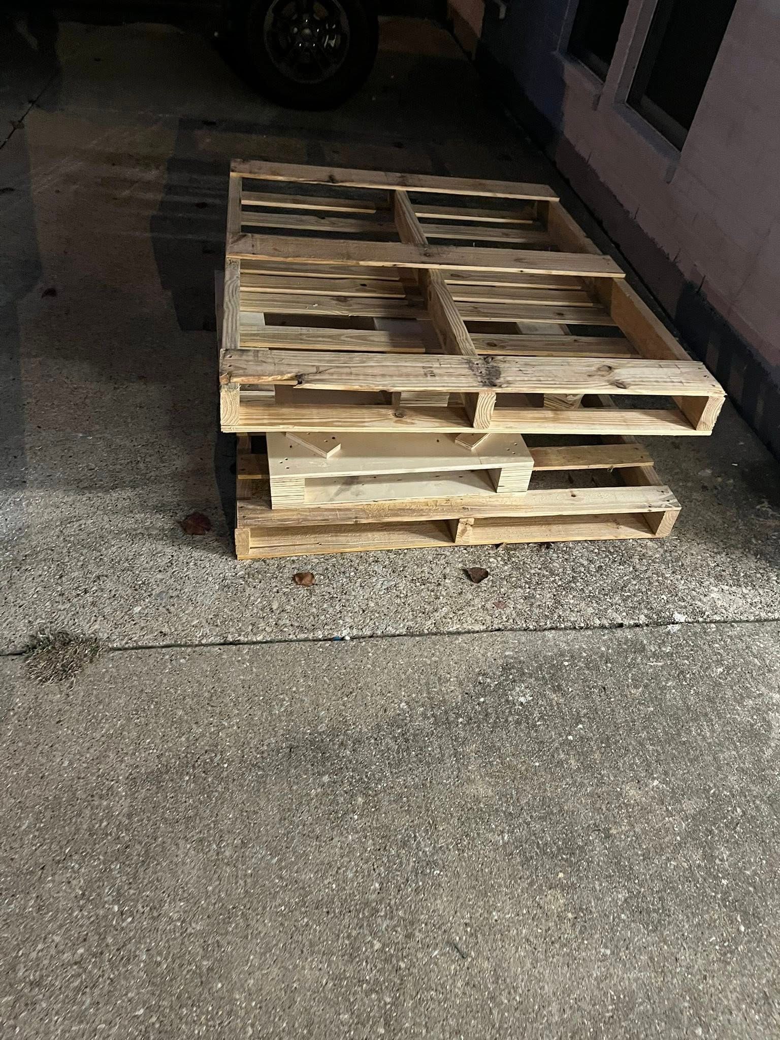 Two wooden pallets stacked on a concrete surface, near a building.