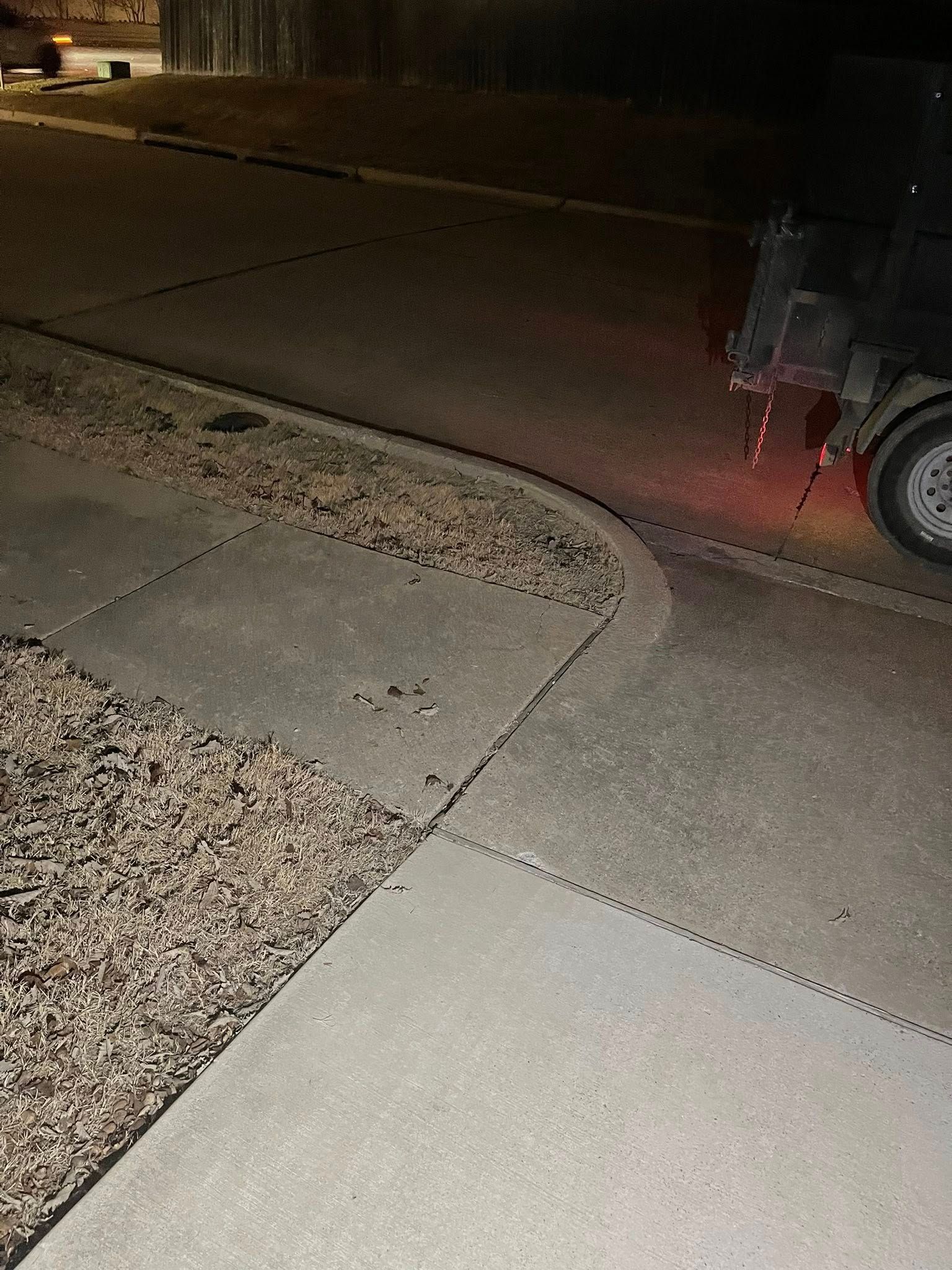 Night sidewalk beside a road, with gravel landscaping and a partial motorcycle at the right edge.