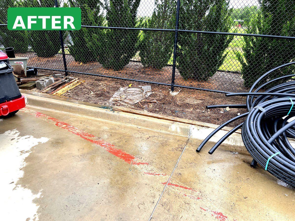 Wet concrete patio with red marking, chain-link fence, plants, and coiled black hoses