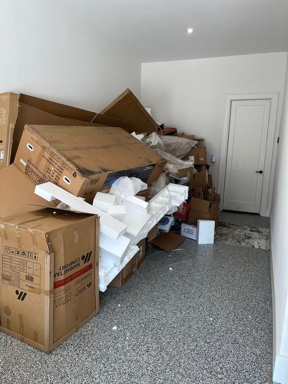 Person bagging trash near a pile of cardboard, mattress, and bags; yard setting.