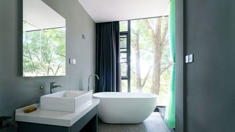 Un bagno moderno con vasca freestanding bianca, lavabo quadrato su mobiletto e un'ampia finestra con vista sugli alberi.