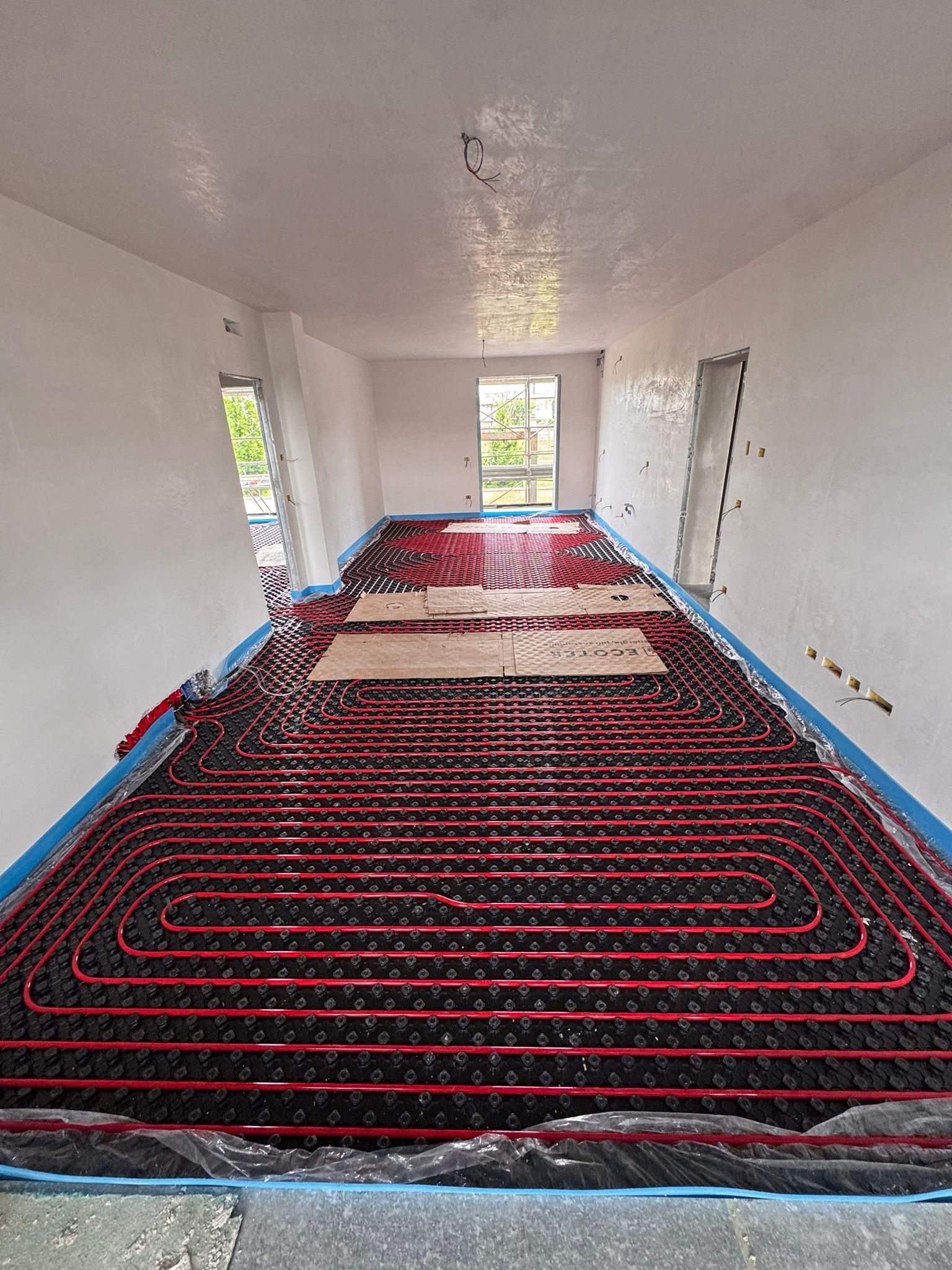 In una stanza in costruzione, tubi rossi per il riscaldamento a pavimento radiante installati a griglia su una base isolante nera.