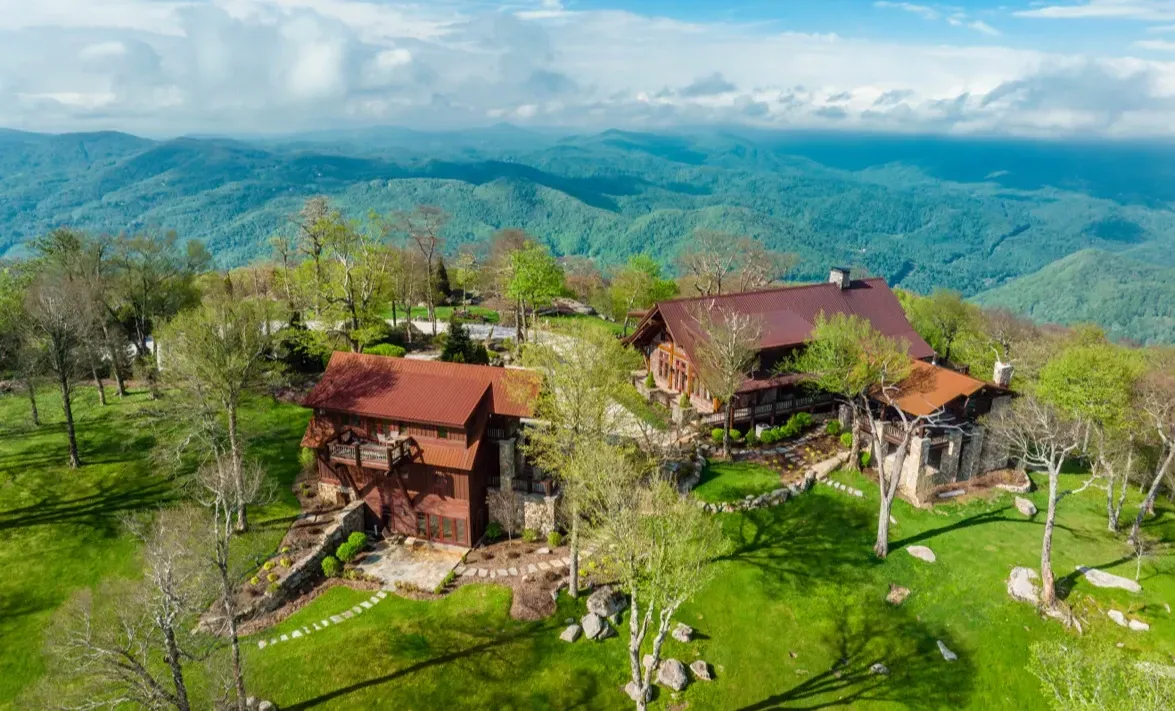 An aerial view of a house on top of a hill with mountains in the background.
