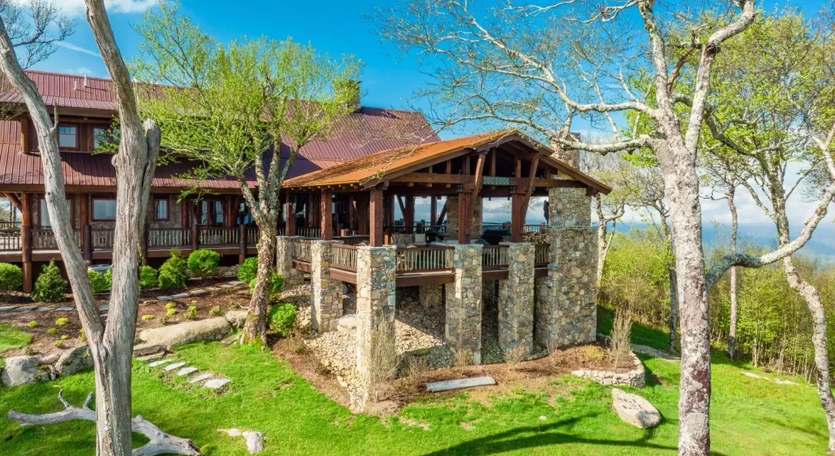 A large house is sitting on top of a lush green hill surrounded by trees.