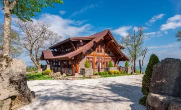 A large wooden house is sitting on top of a hill surrounded by trees and rocks.