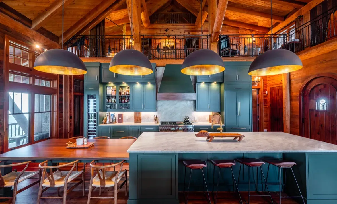 A kitchen with green cabinets , a large island , a table and chairs.