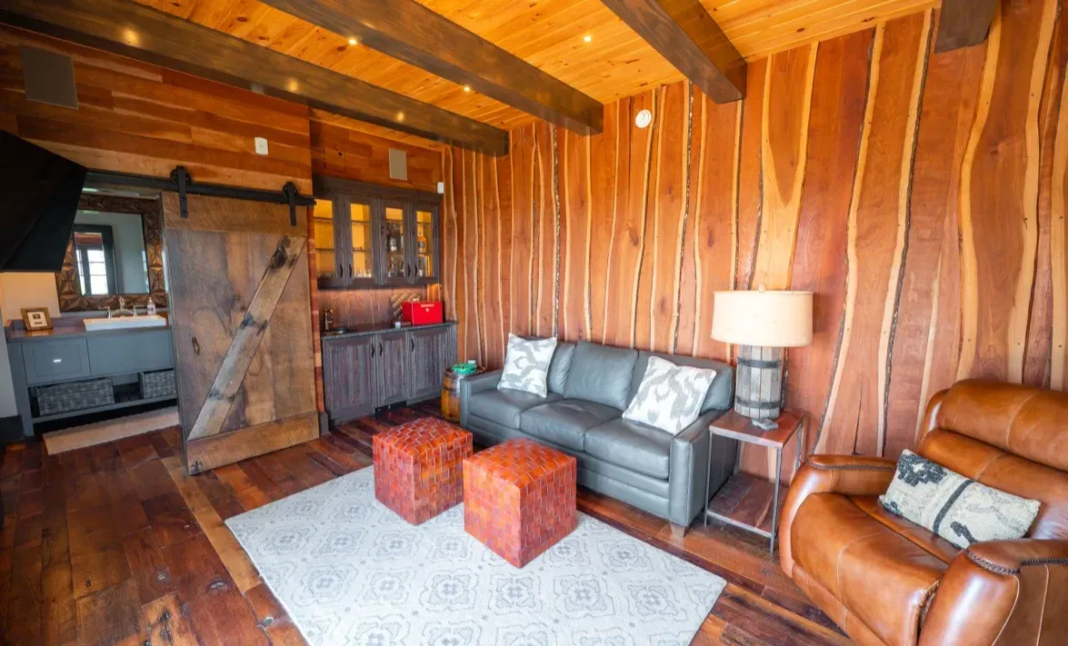 A living room with a couch , chairs , ottomans and a sliding barn door.