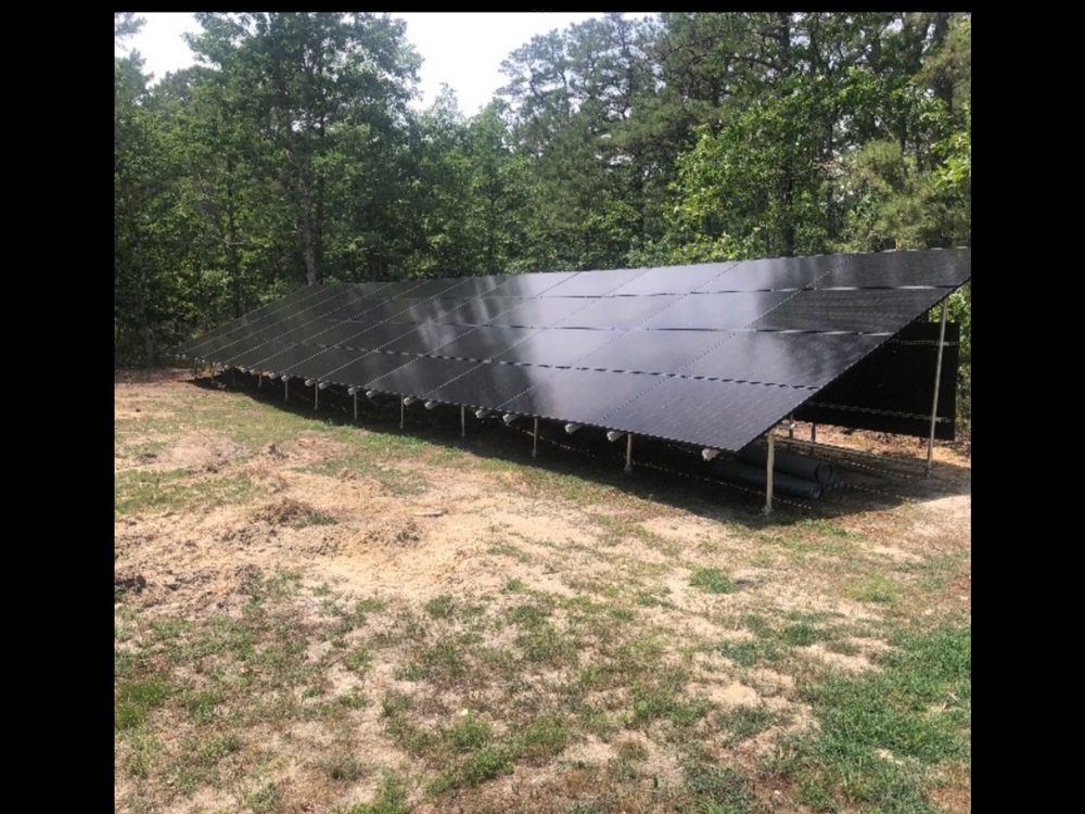 Solar panels on a metal frame in a grassy field with trees in the background.