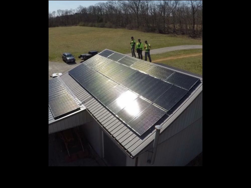 Solar panels installed on a building roof; three people in high-vis vests on the roof. Sunny day.
