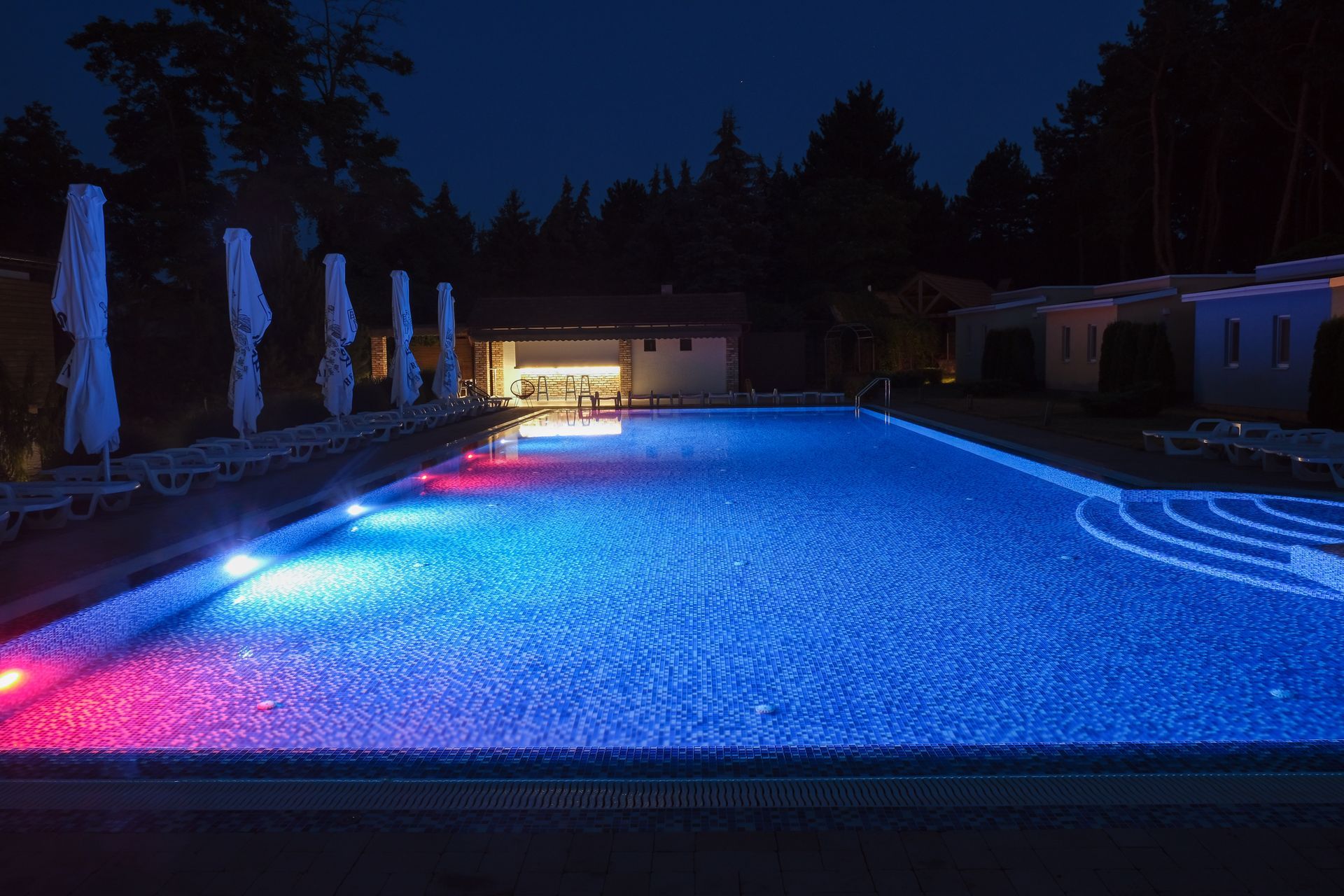 A large swimming pool is lit up at night with colorful lights.