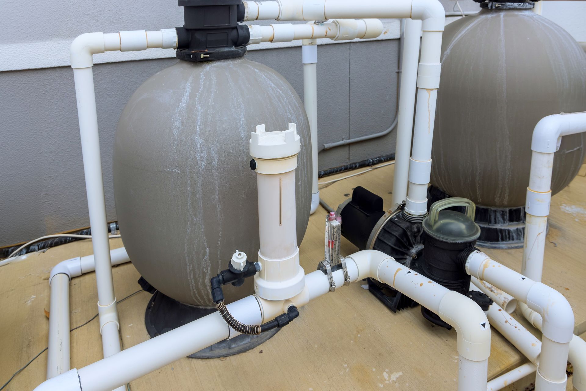 A swimming pool filter is surrounded by white pipes.