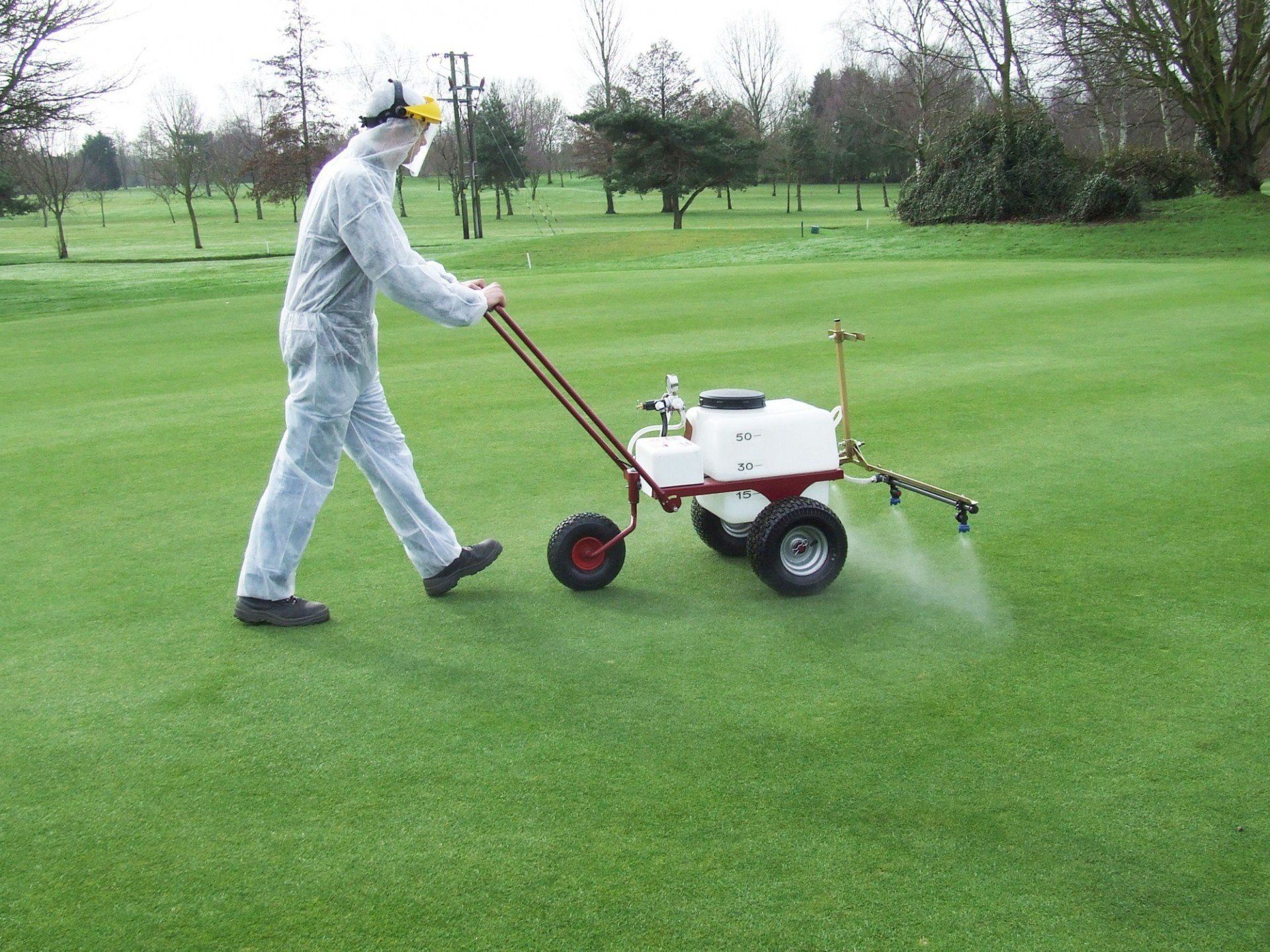 man walking golf course spraying fertilizer