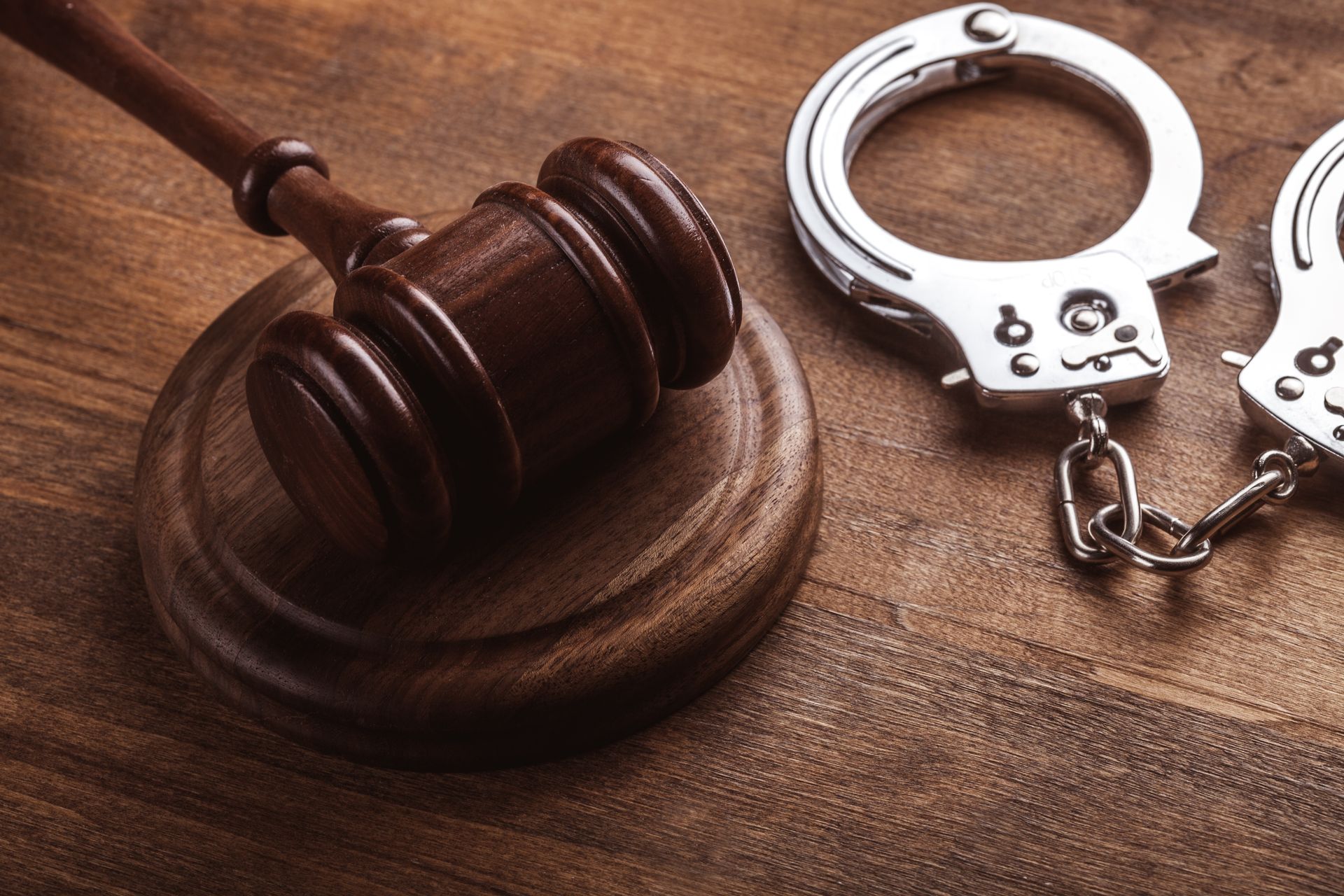 A wooden judge 's gavel and handcuffs on a wooden table.