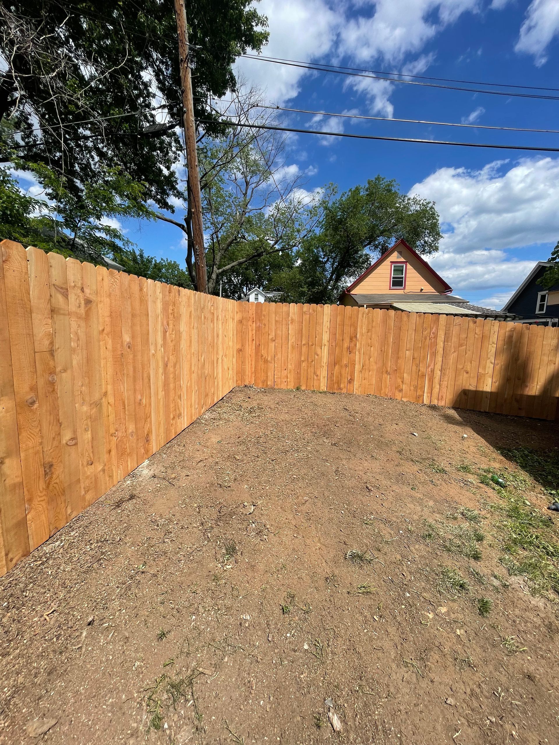A wooden fence surrounds a dirt yard with a house in the background.