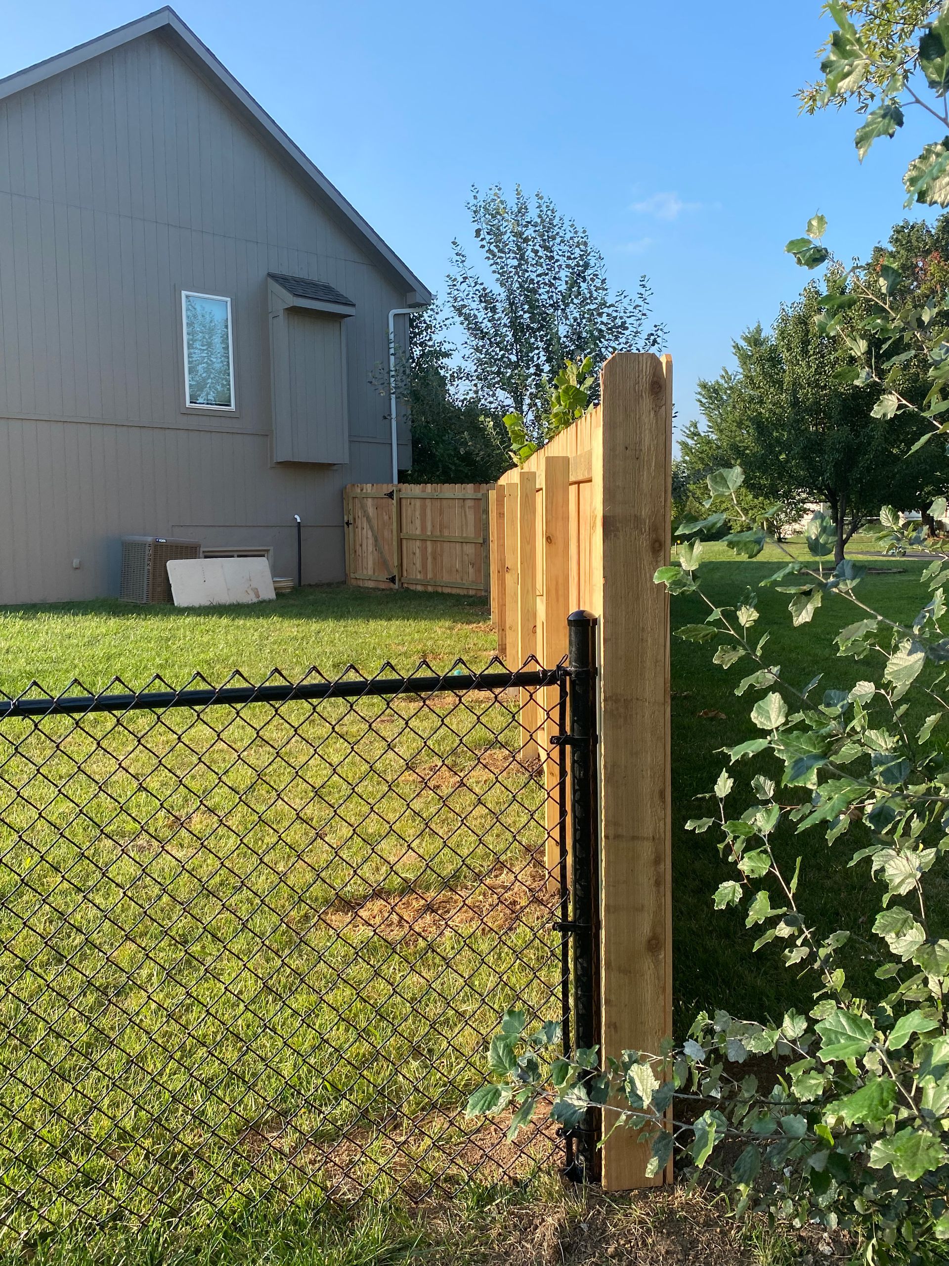 A wooden fence with a chain link fence in front of a house.
