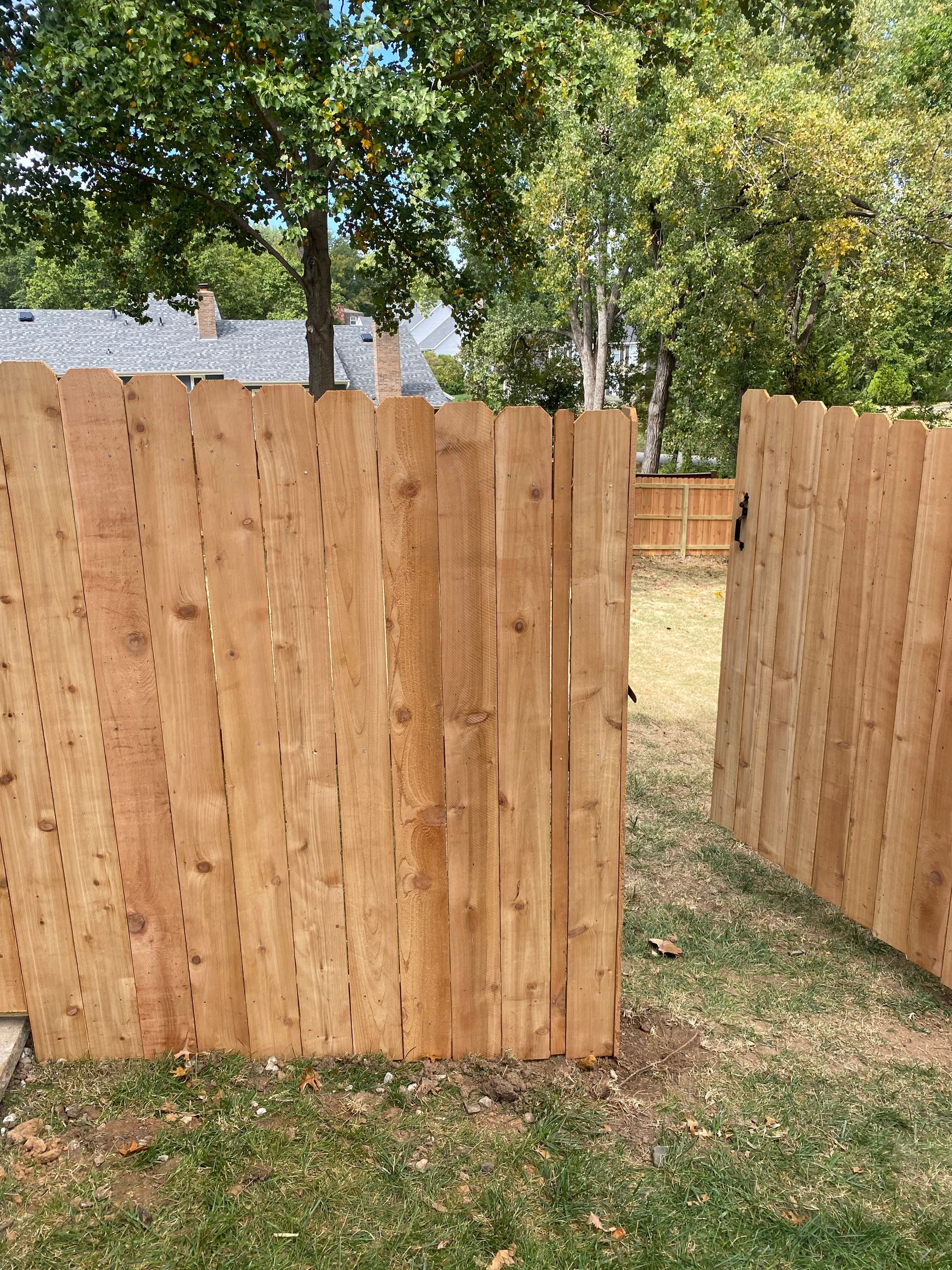 A wooden fence is surrounded by grass and trees in a yard.