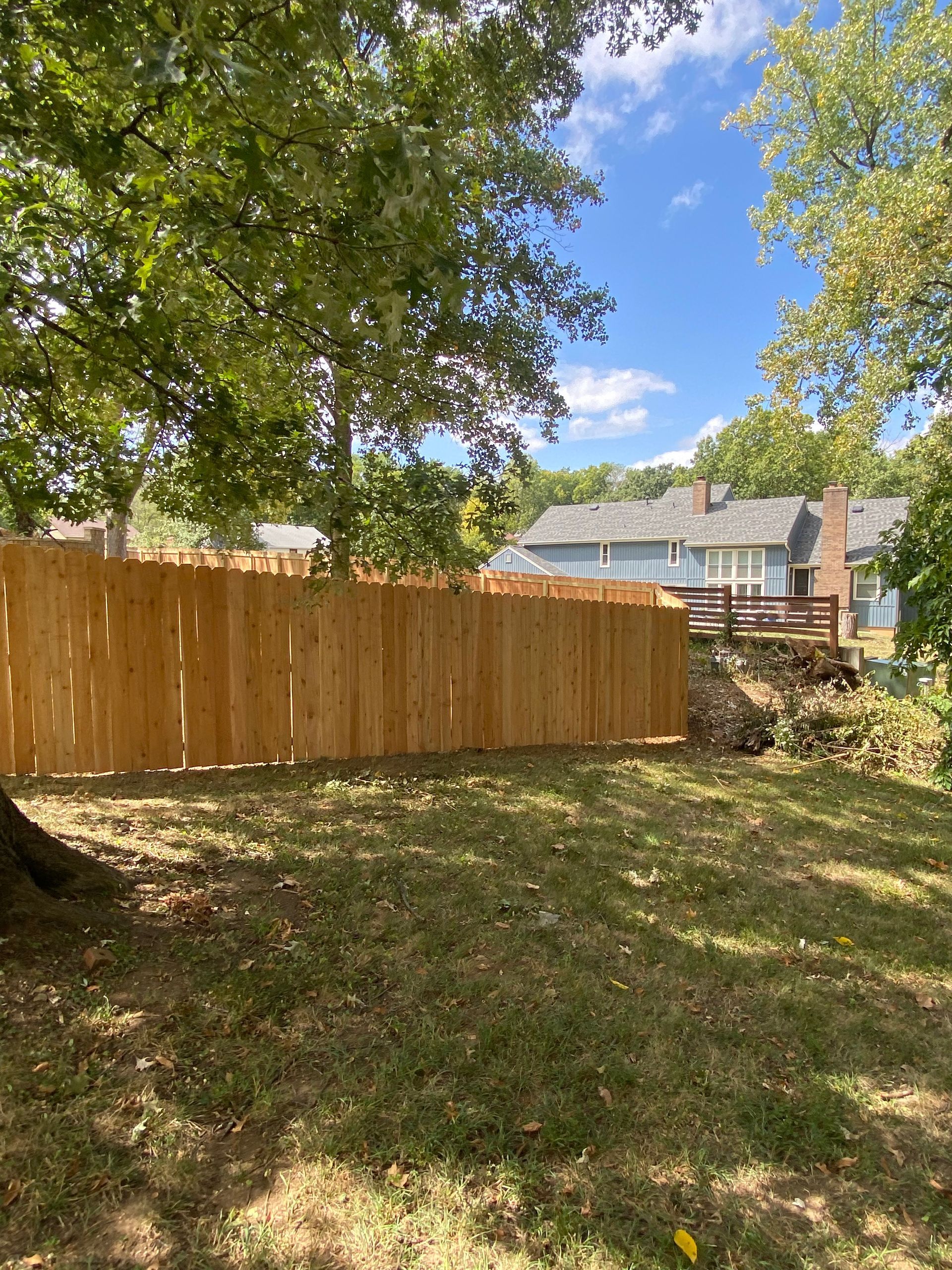 A wooden fence in a backyard with a house in the background.