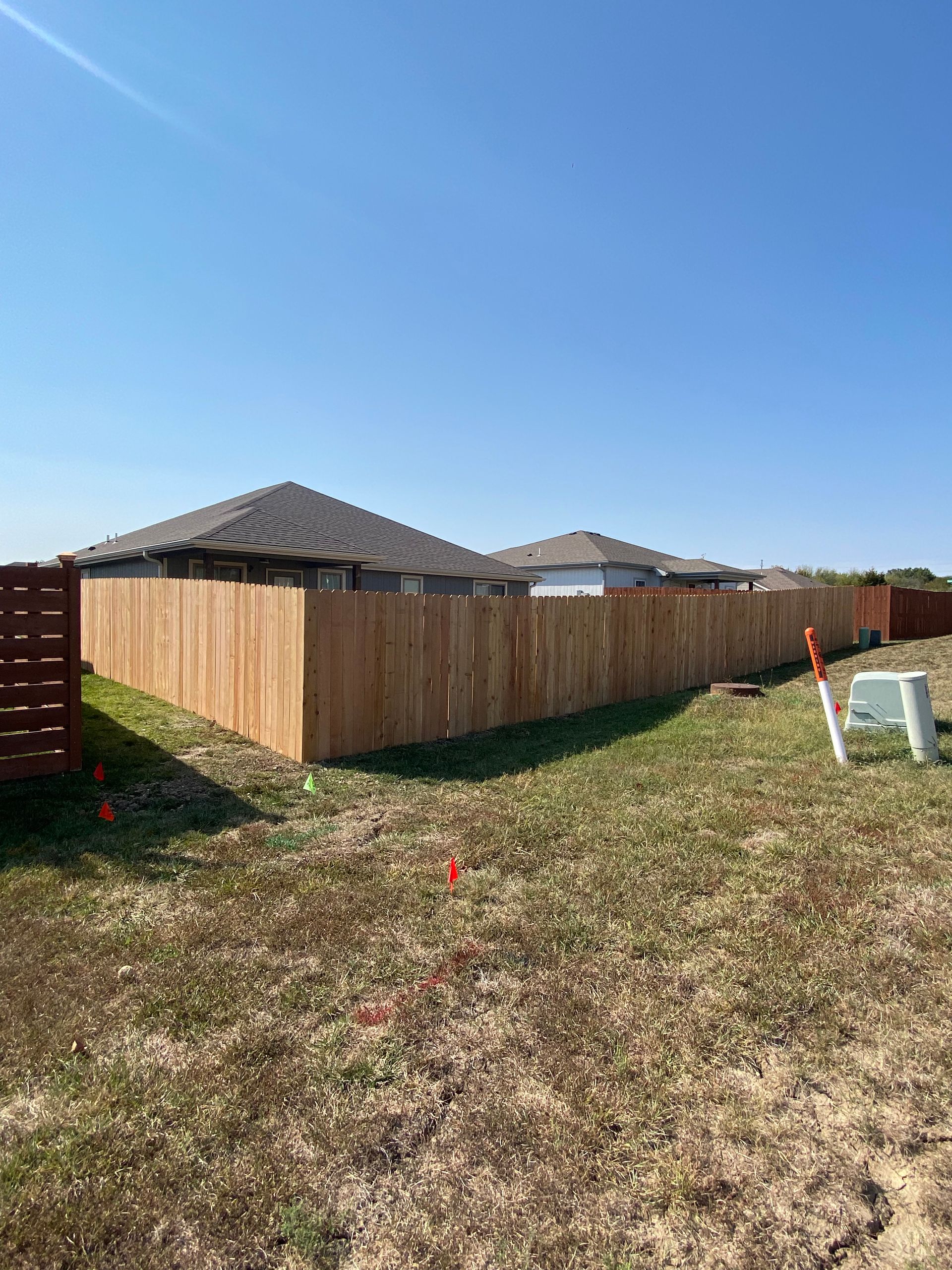 A wooden fence is in the middle of a grassy field in front of a house.