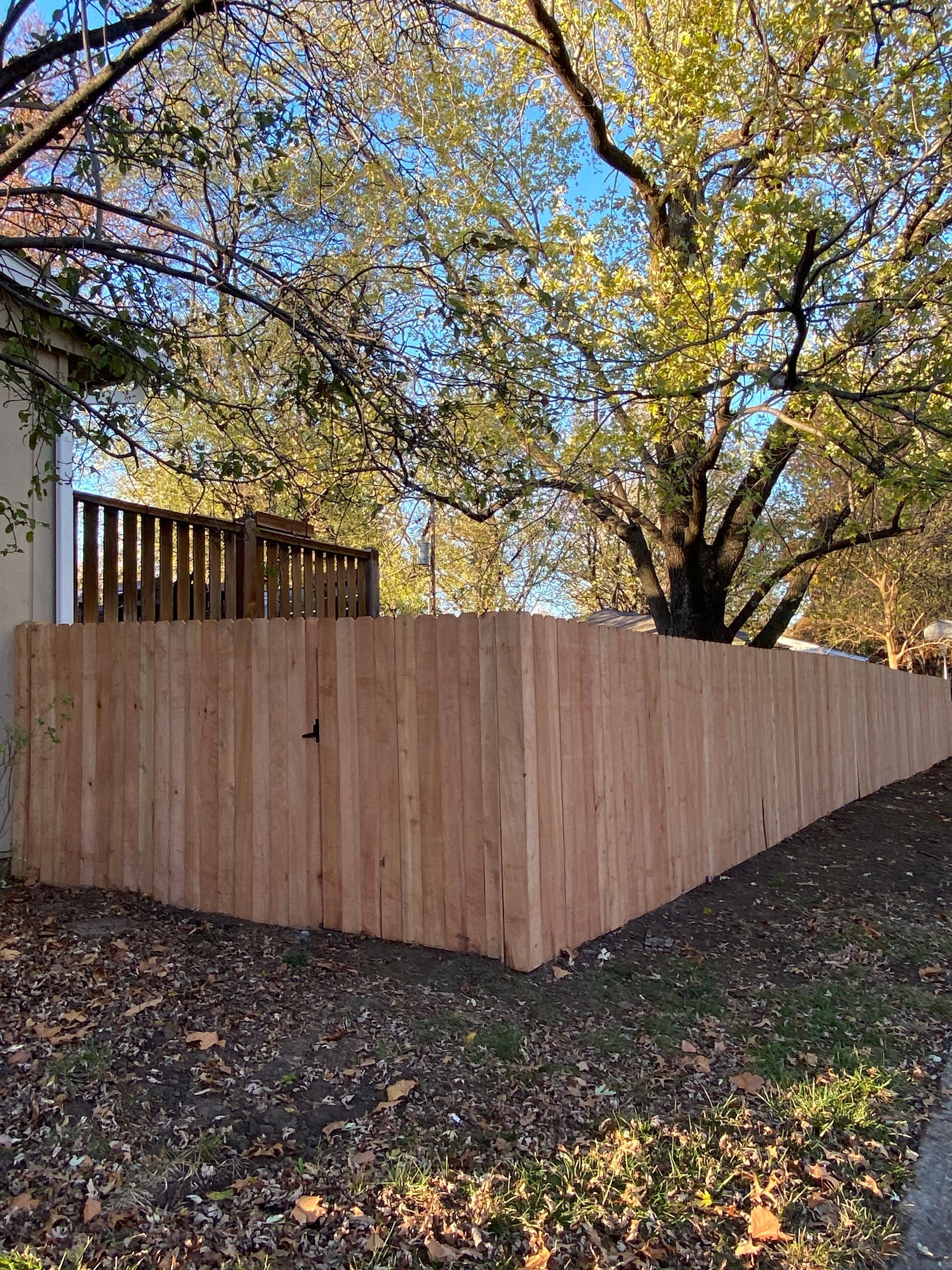 A wooden fence is surrounded by trees and leaves in front of a house.