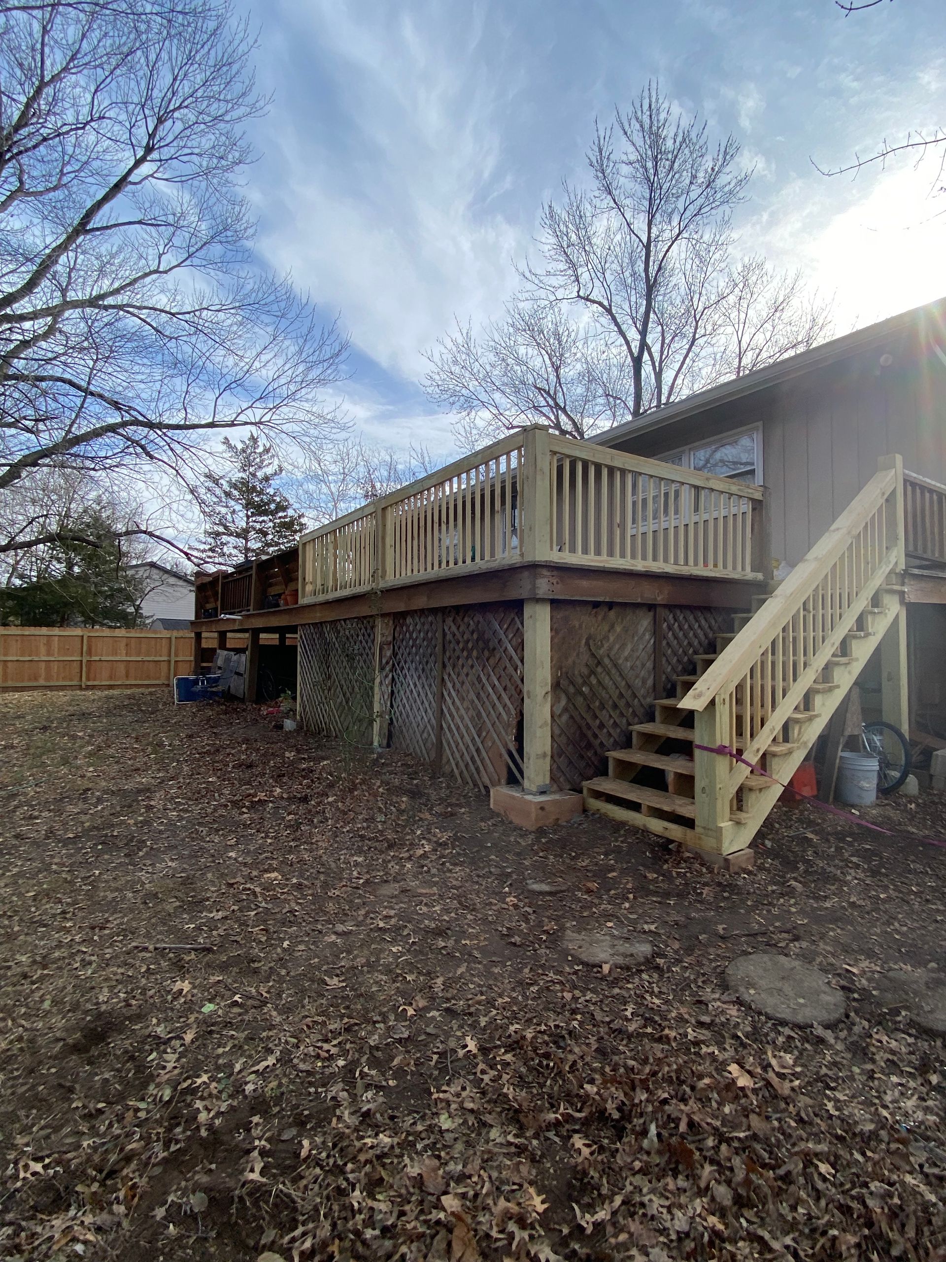 A wooden deck with stairs leading up to it is in the backyard of a house.