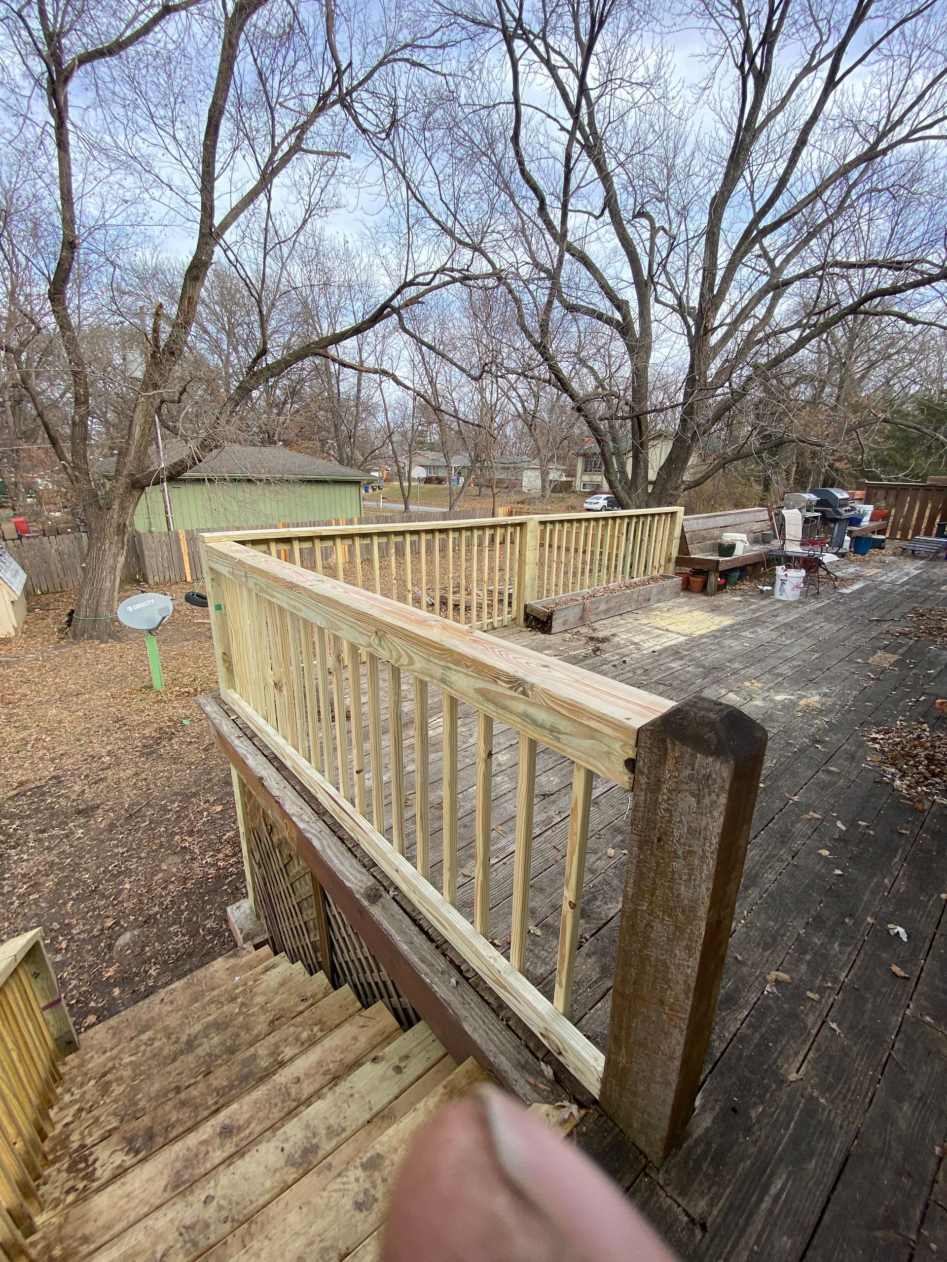 A person is standing on a wooden deck with stairs leading up to it.