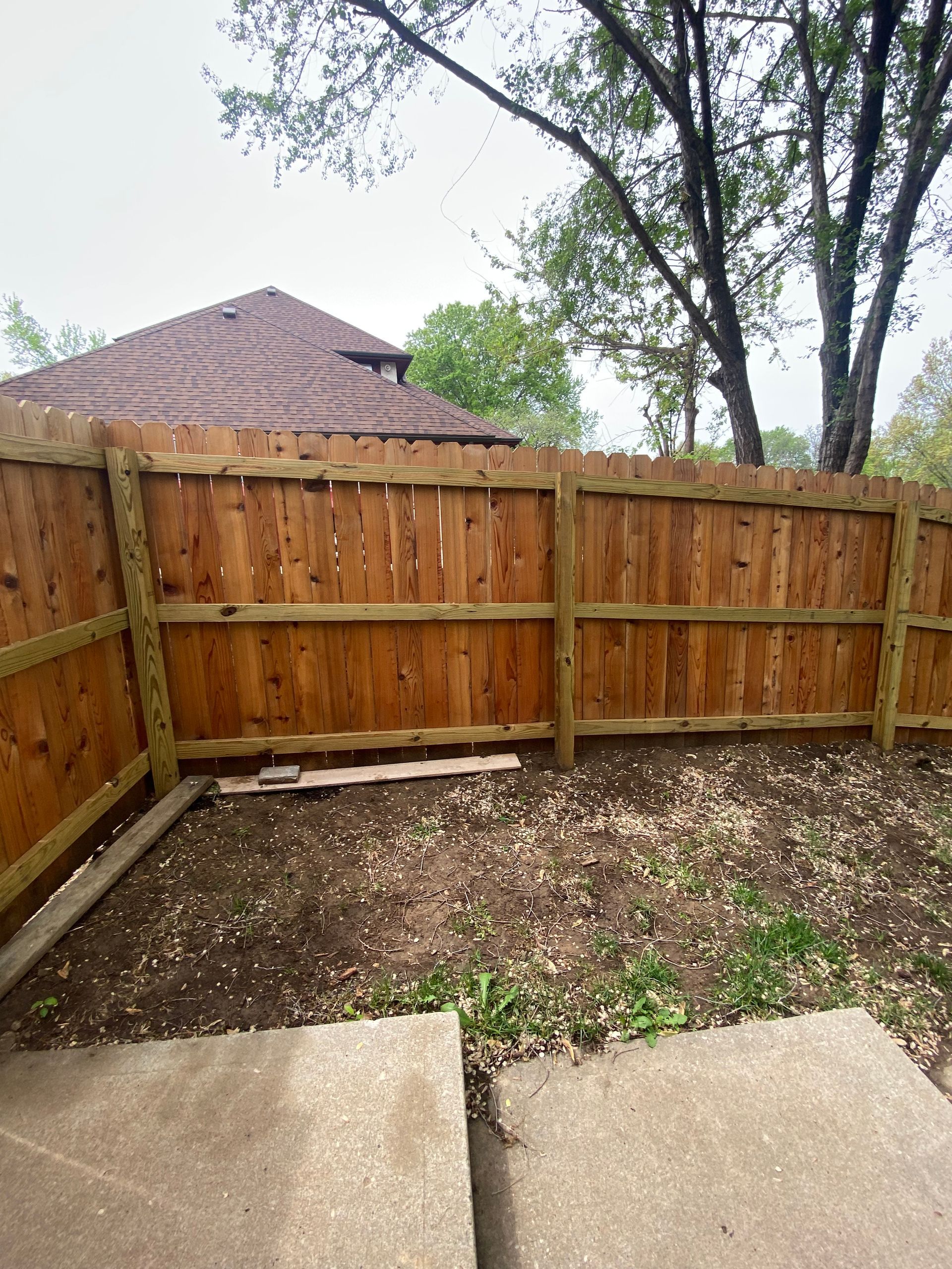 A wooden fence in a backyard with a house in the background.