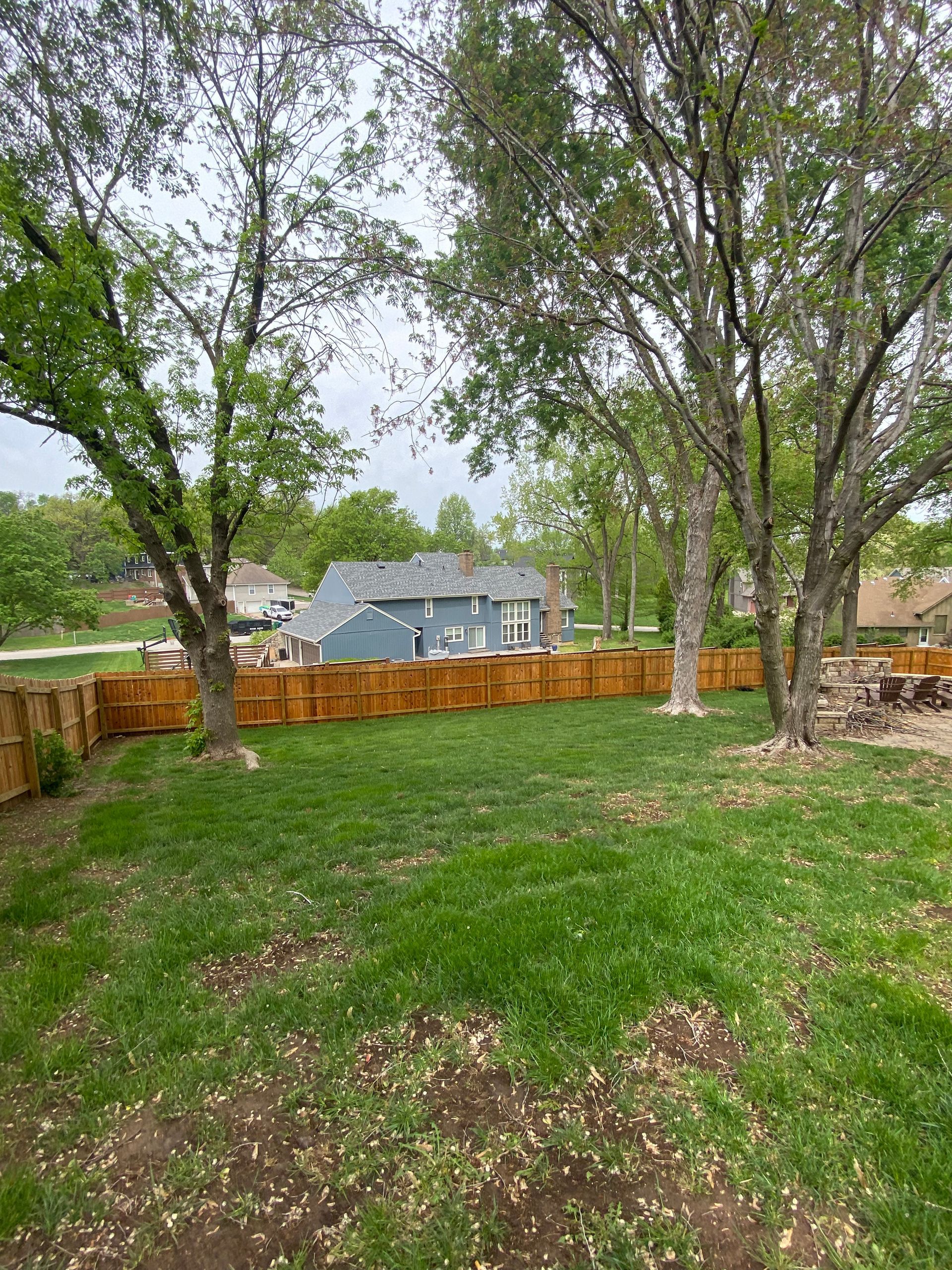 A backyard with a wooden fence and a house in the background.