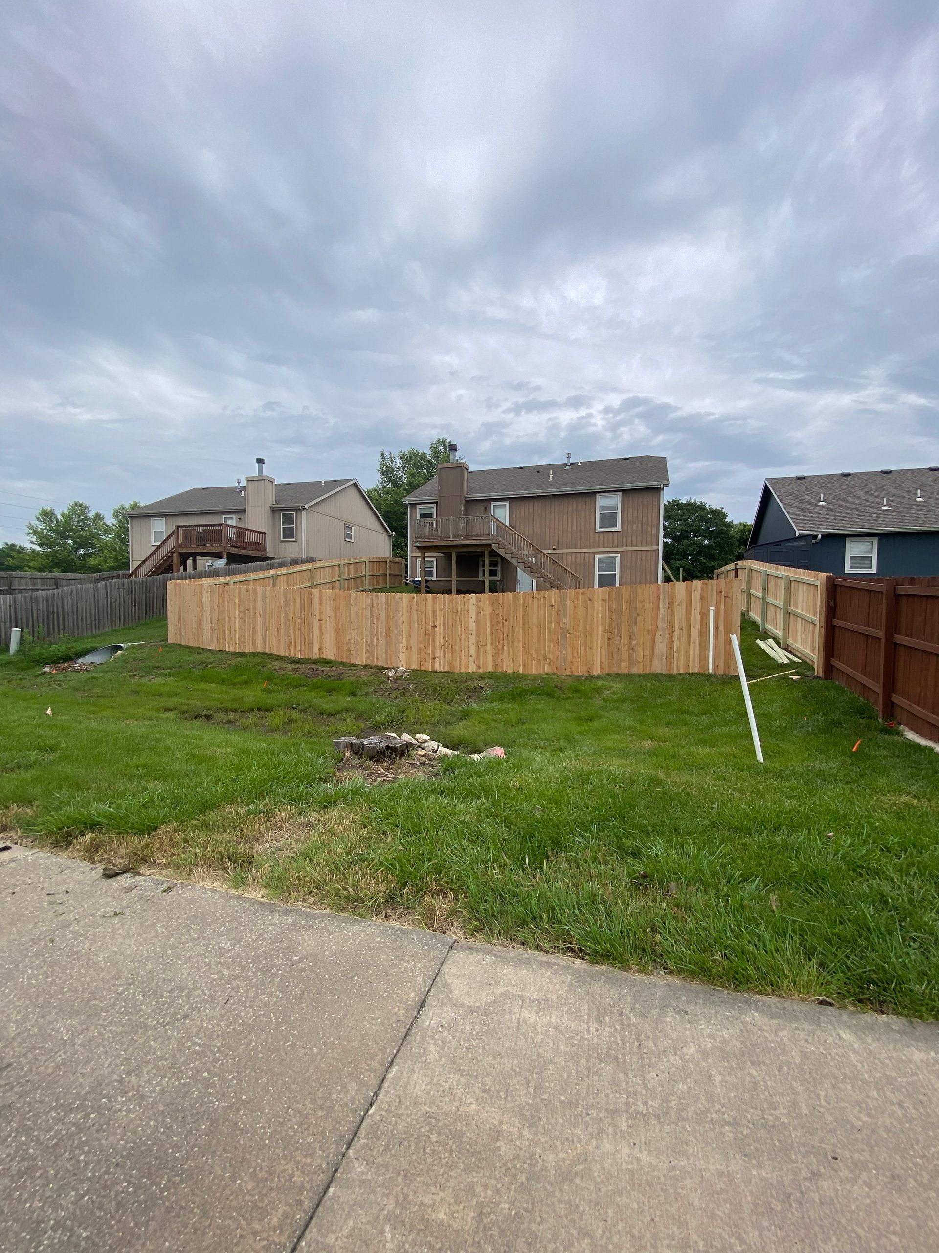 A wooden fence surrounds a grassy yard in front of a house.