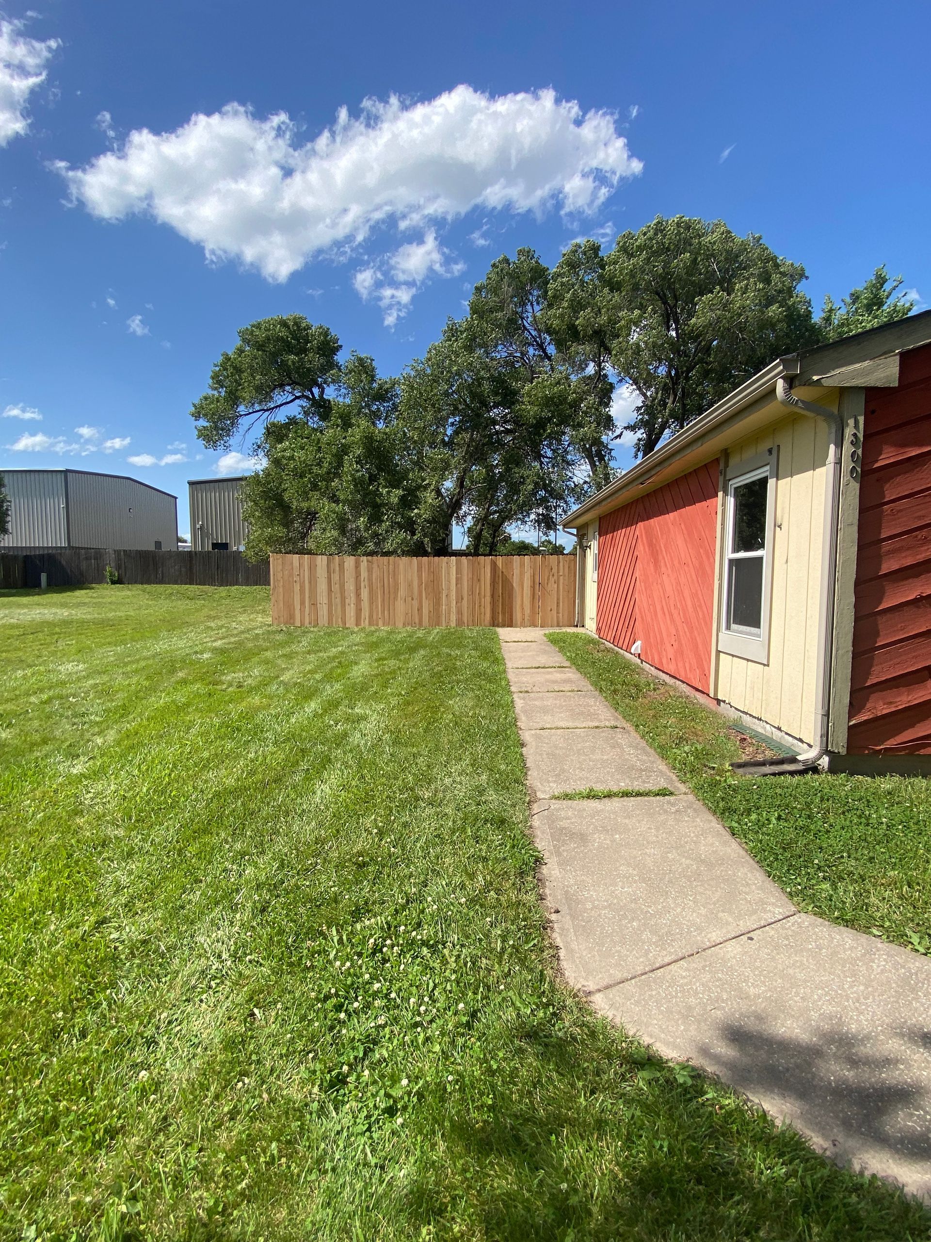 A sidewalk leading to a house with a wooden fence in the backyard.