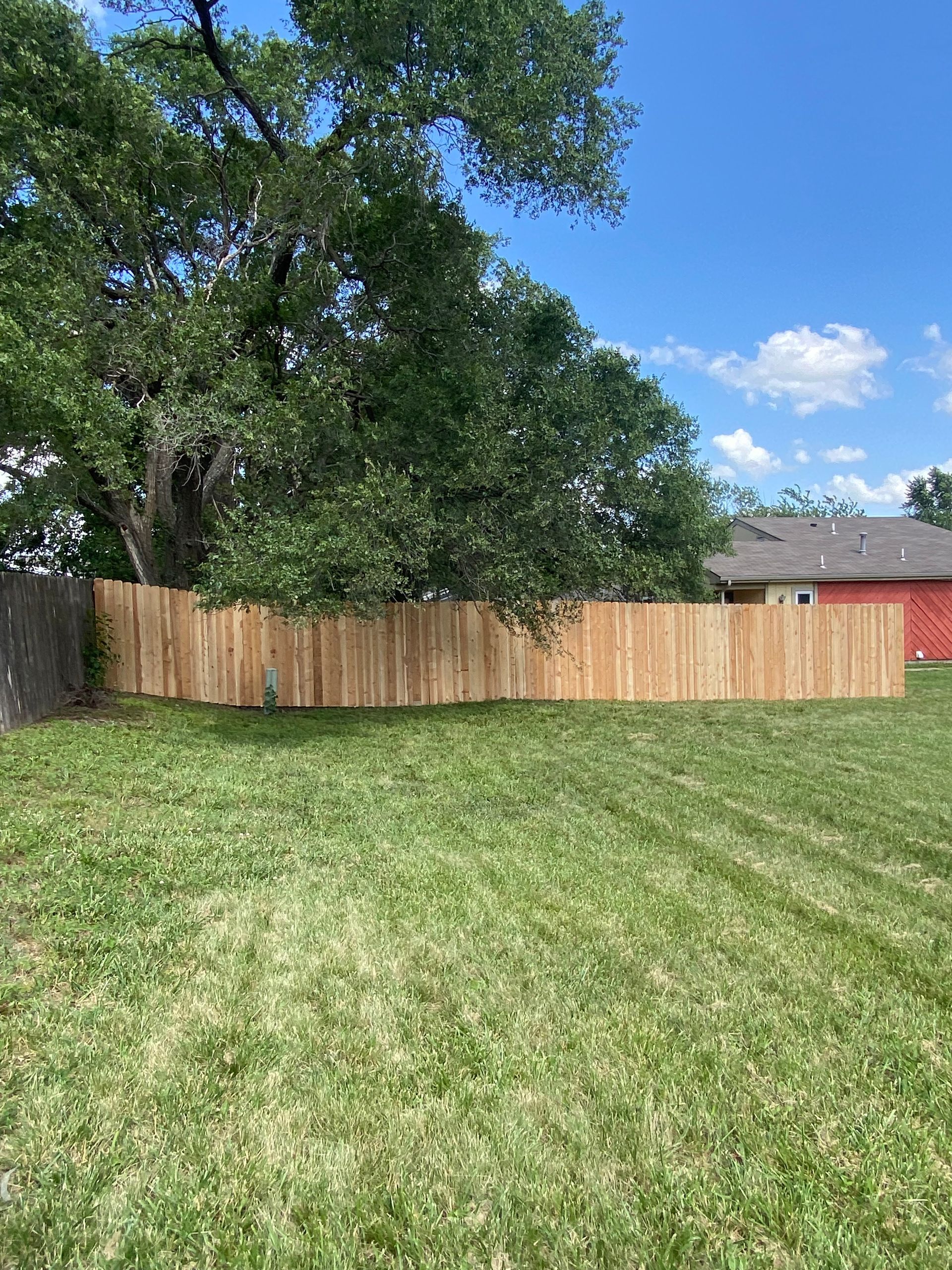 A wooden fence is in the middle of a lush green yard.