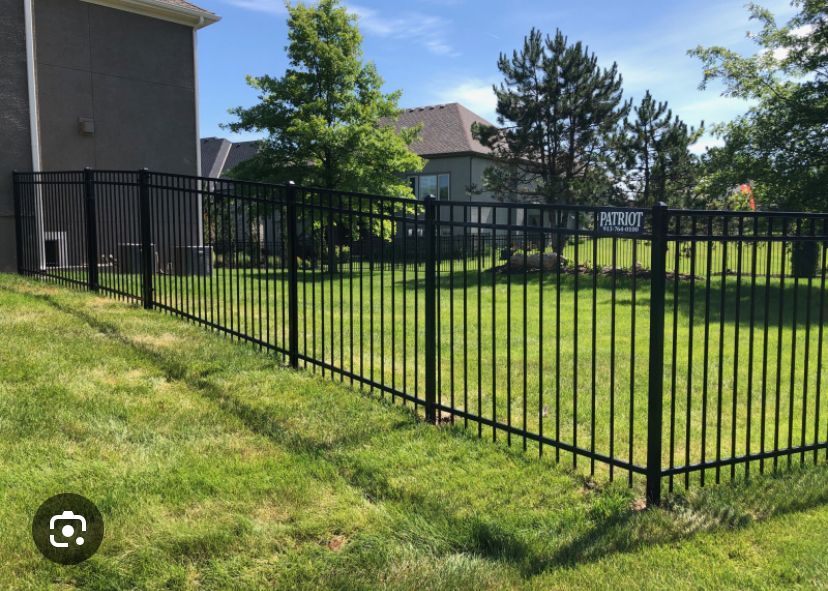 A black metal fence surrounds a lush green yard in front of a house.