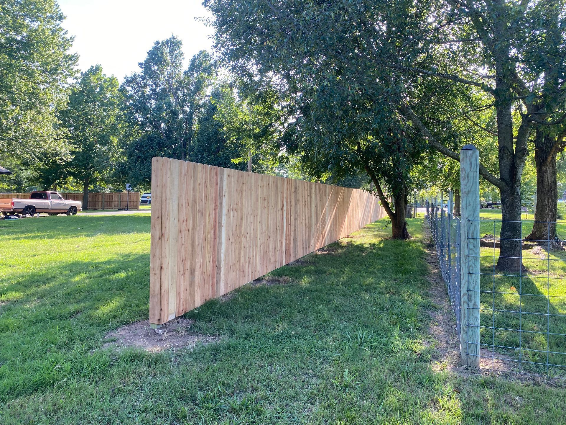A wooden fence is sitting in the middle of a grassy field next to a chain link fence.