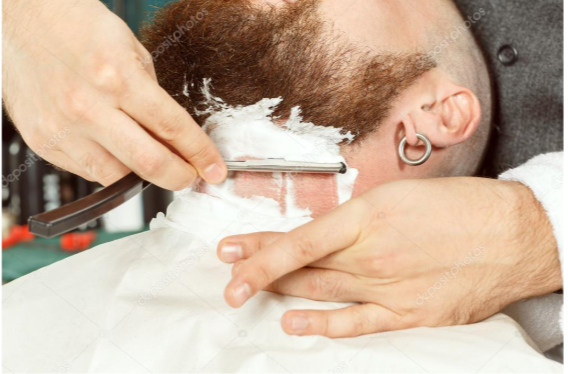 A man is getting his beard shaved by a barber with a razor.