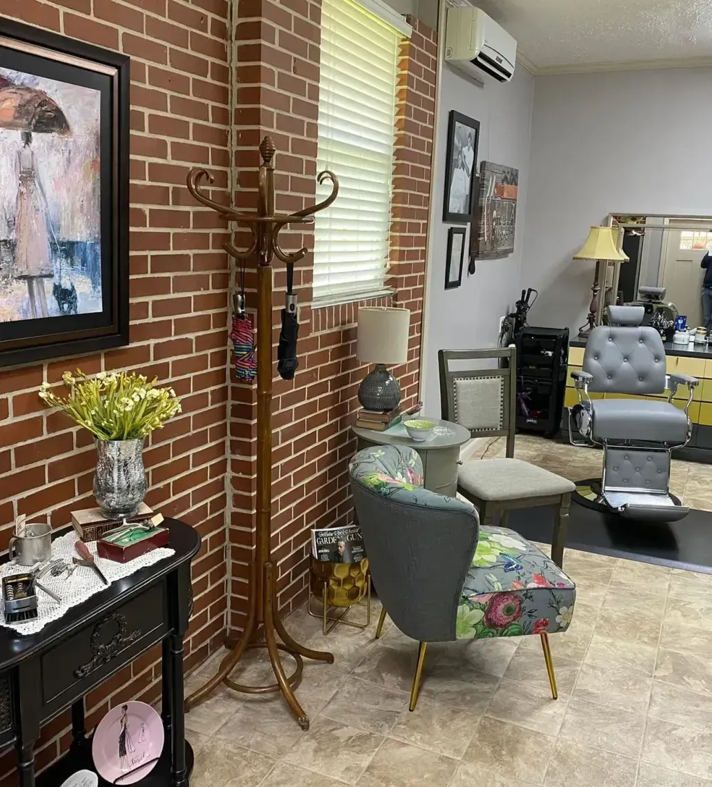 A living room with a brick wall , chairs , lamps and a painting on the wall.
