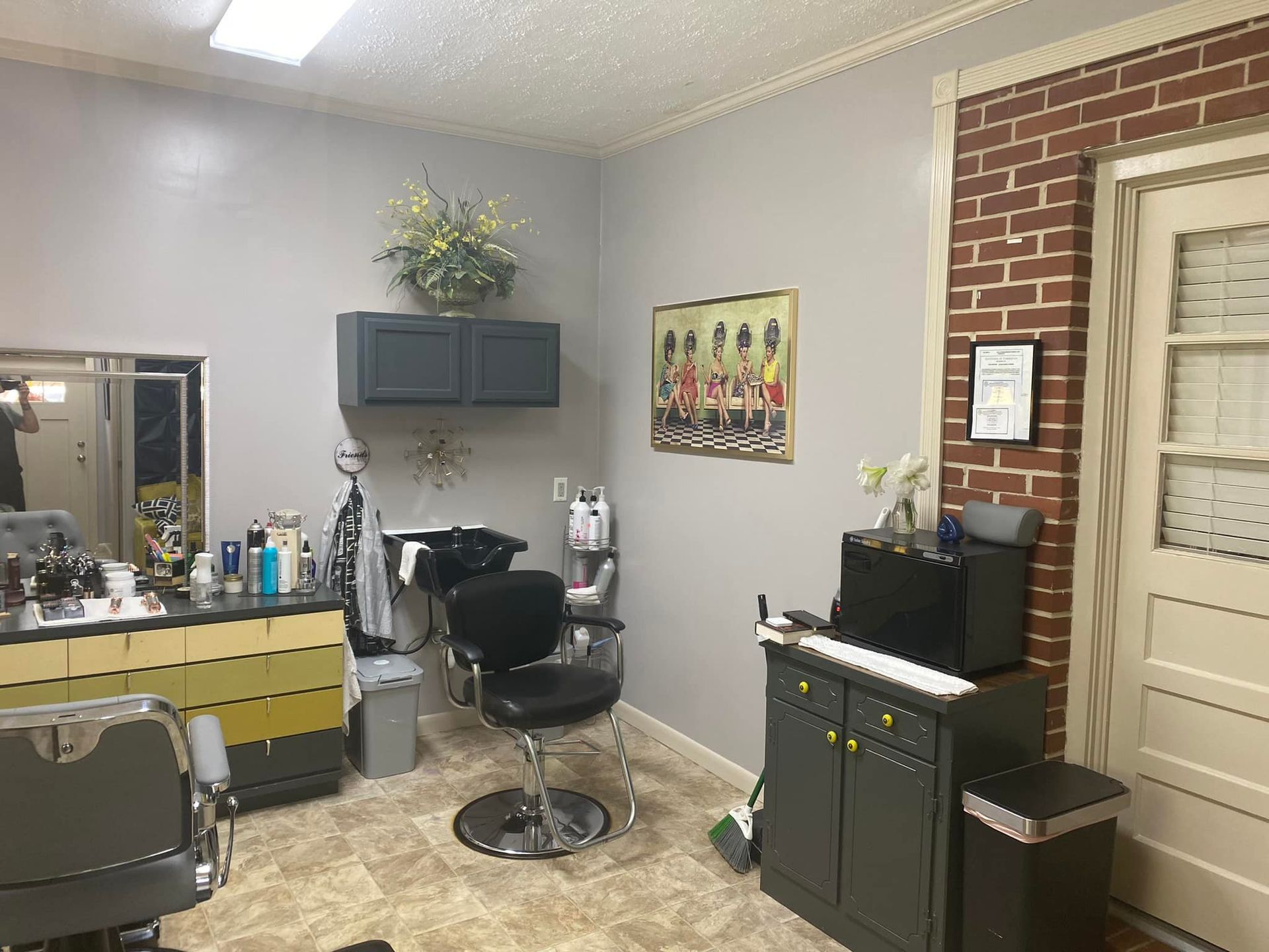 A hair salon with a chair , sink , mirror and cabinets.