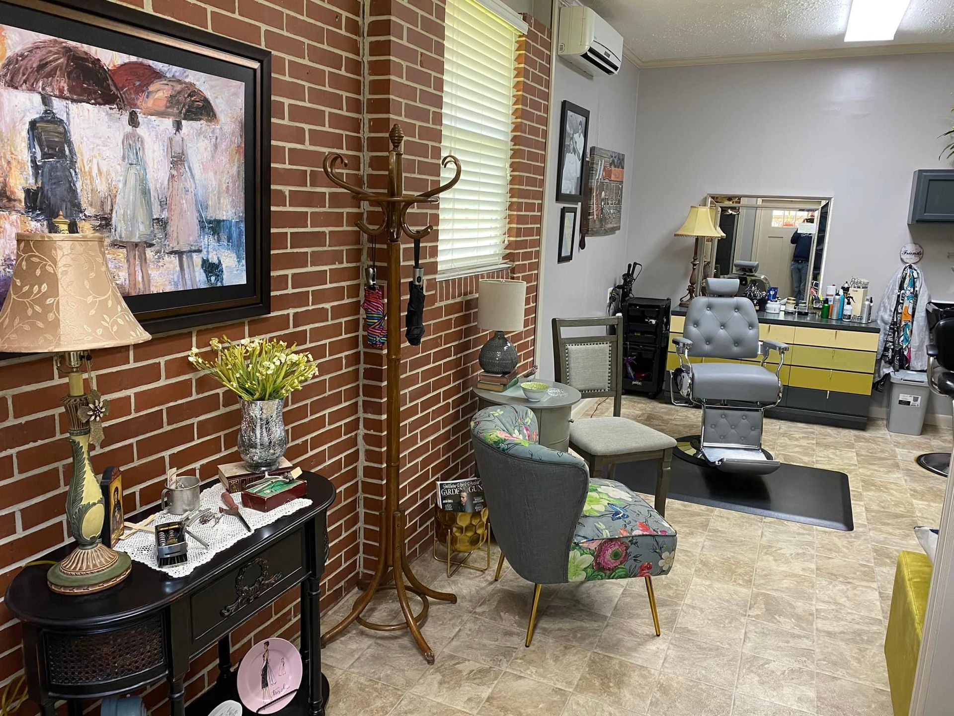 A living room with a brick wall , chairs , lamps and a painting on the wall.