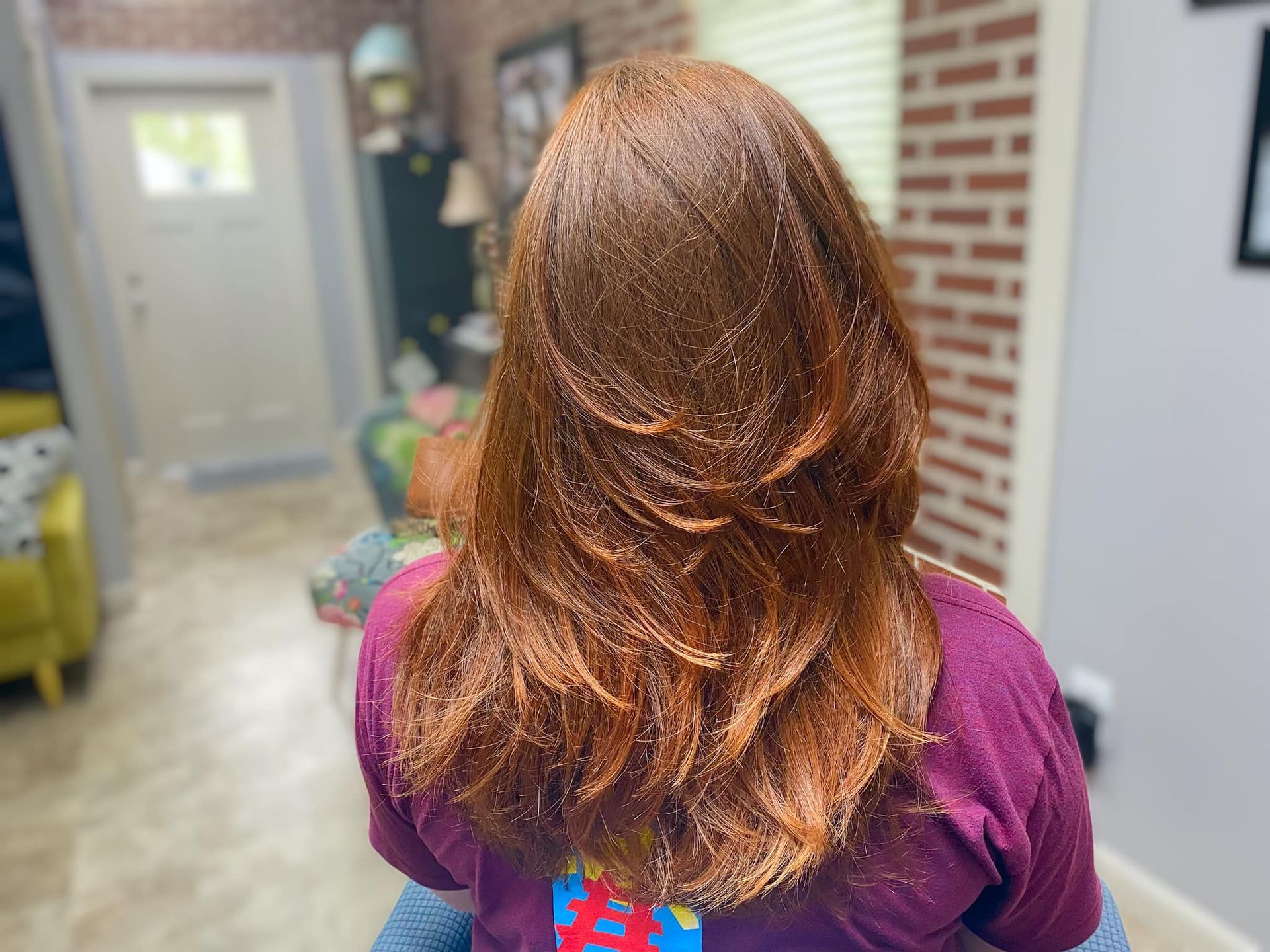 A woman with long red hair is wearing a purple shirt.