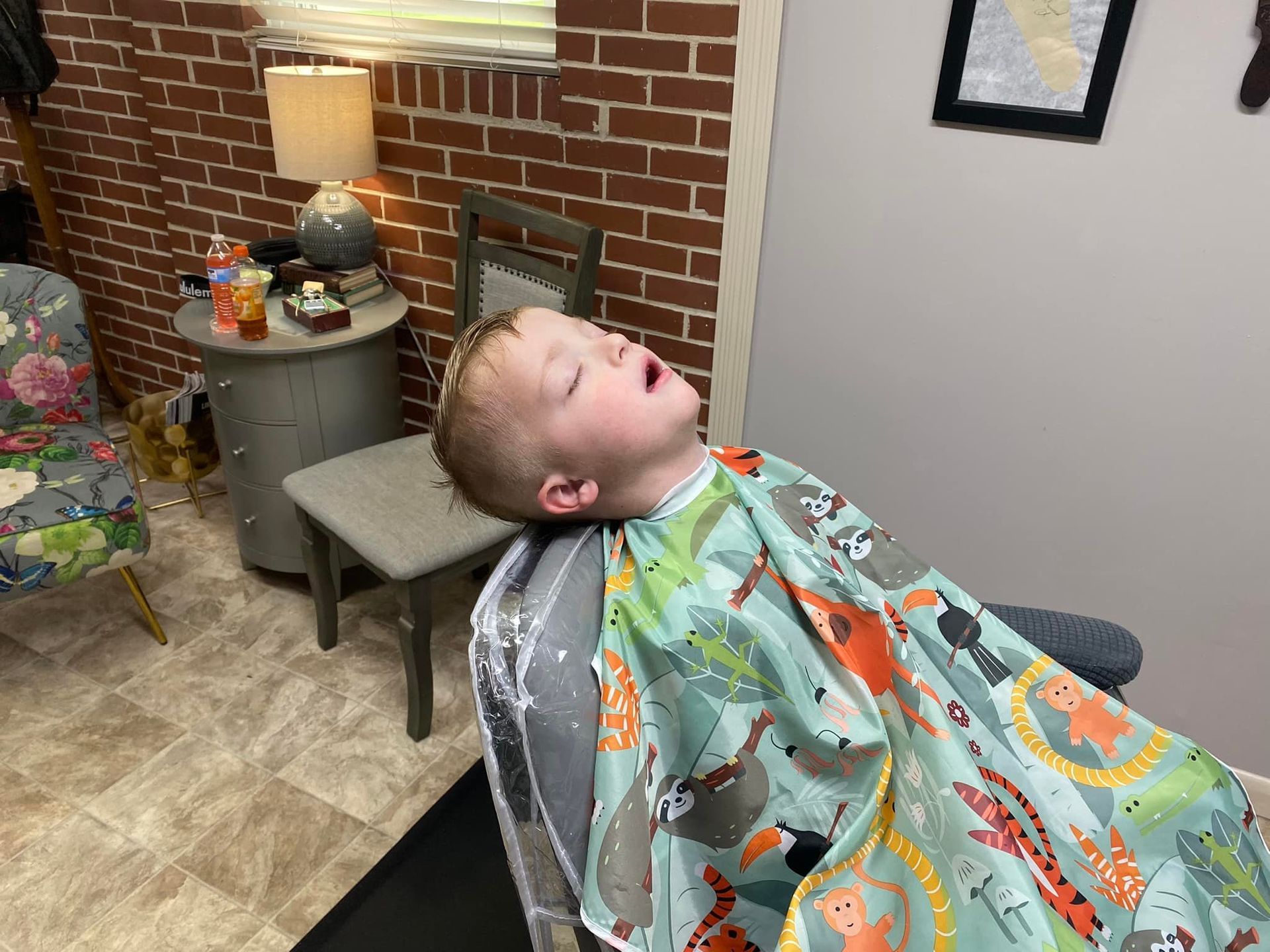 A young boy is laying in a chair in a barber shop with his mouth open.