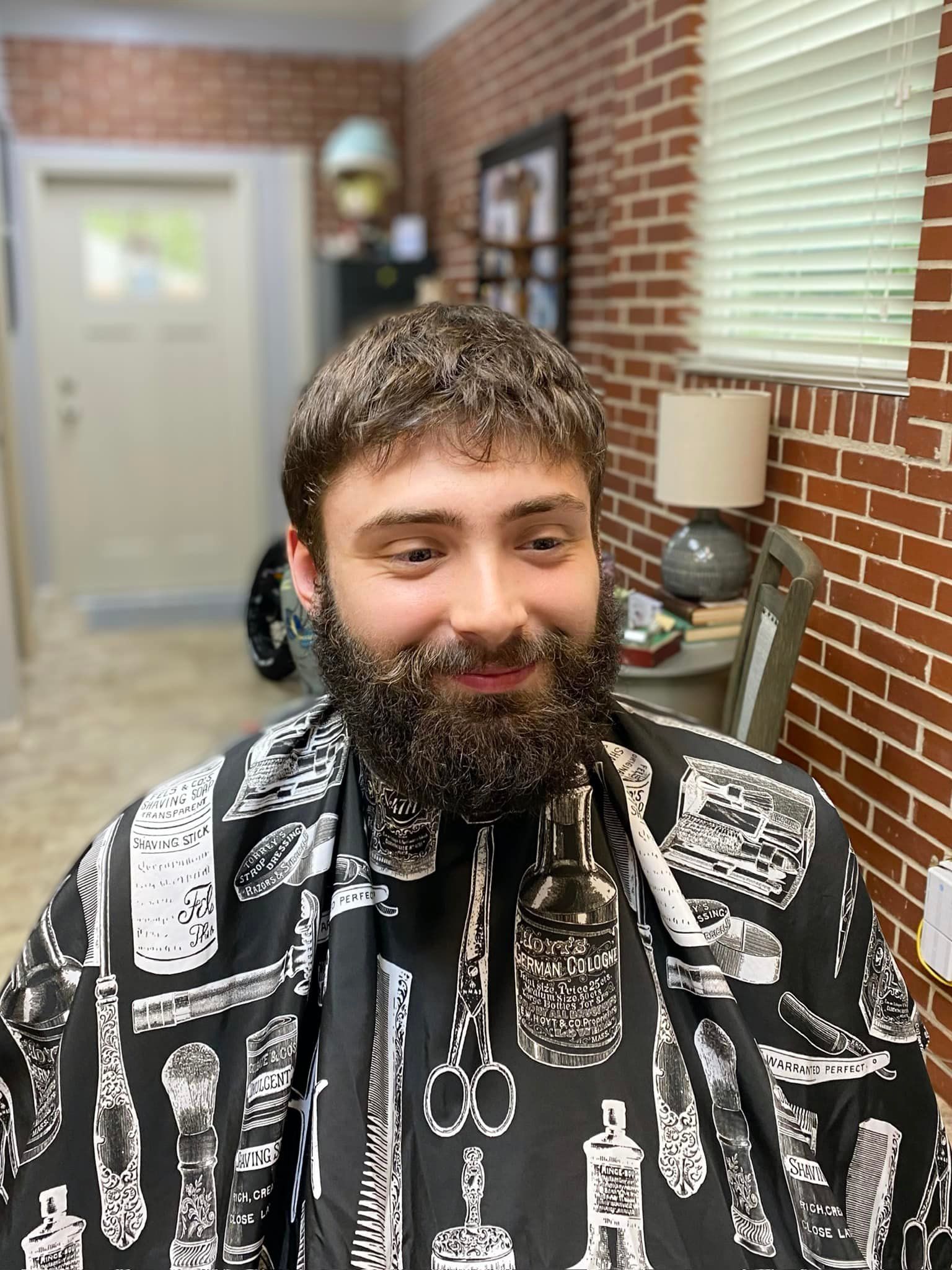 A man with a beard is sitting in a room with a brick wall.